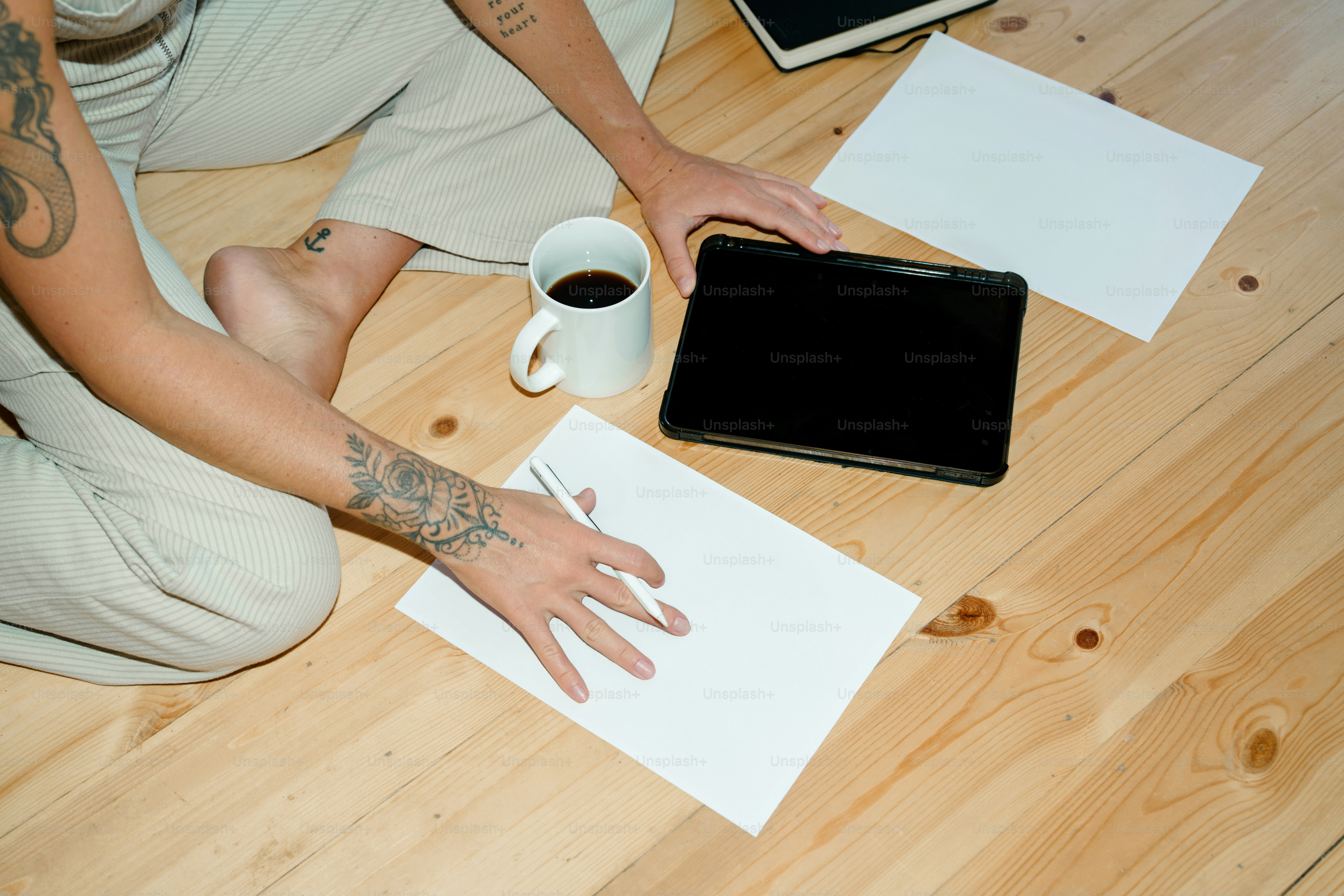 Person writing on paper with coffee and tablet.