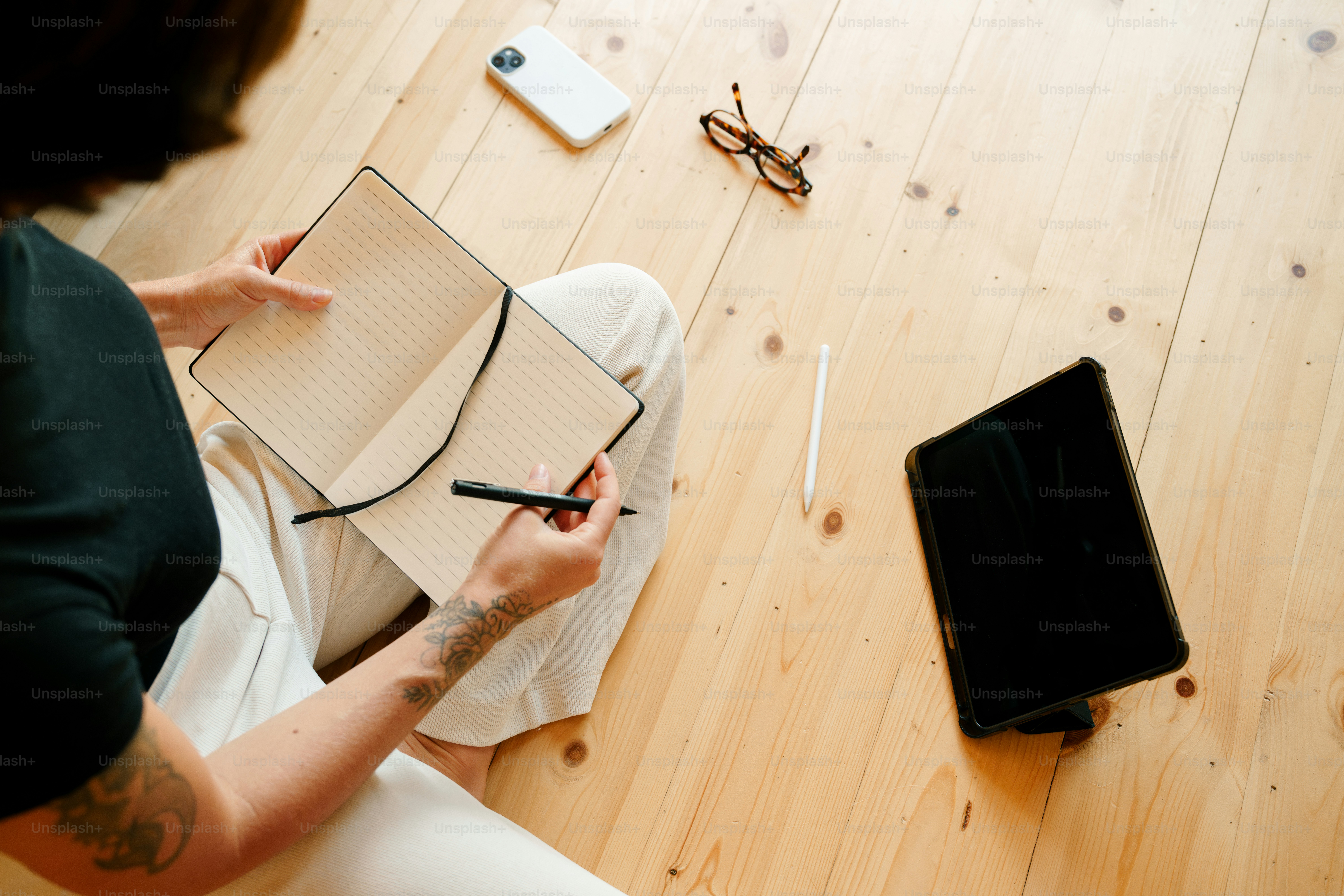 Persona che scrive nel taccuino con tablet e telefono nelle vicinanze.