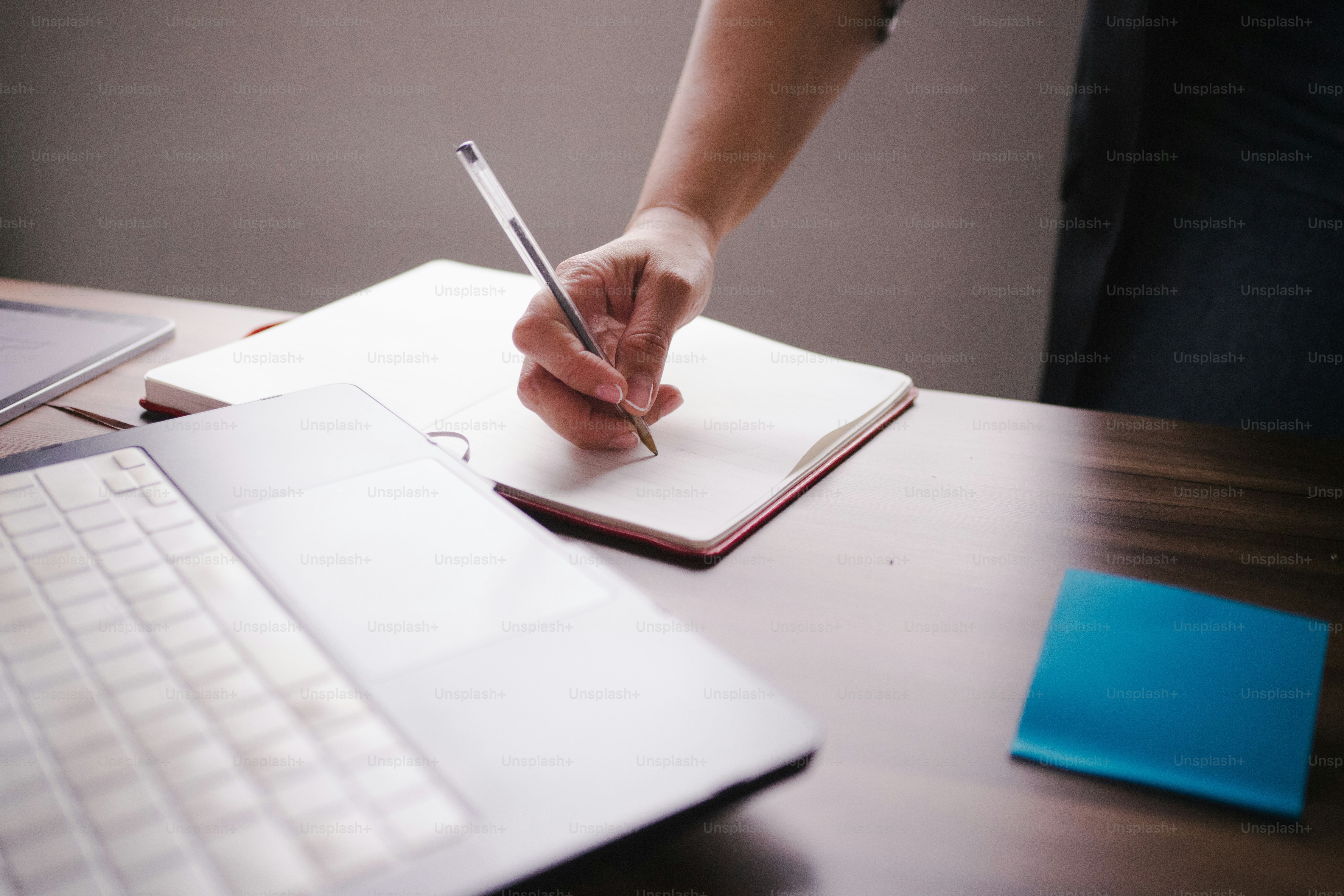 Person writing in notebook next to laptop and sticky note photo ...