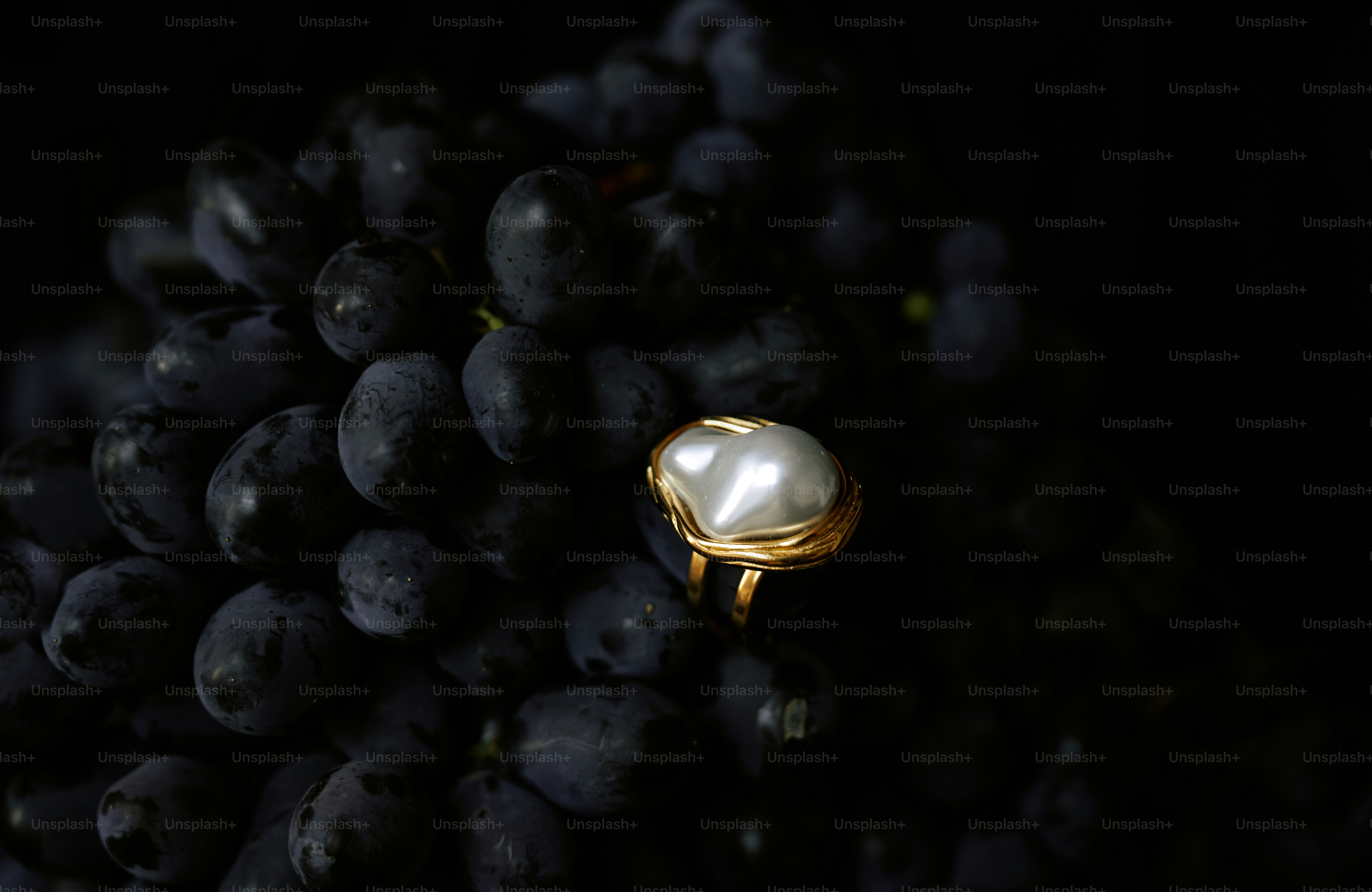 A pearl ring rests on dark grapes