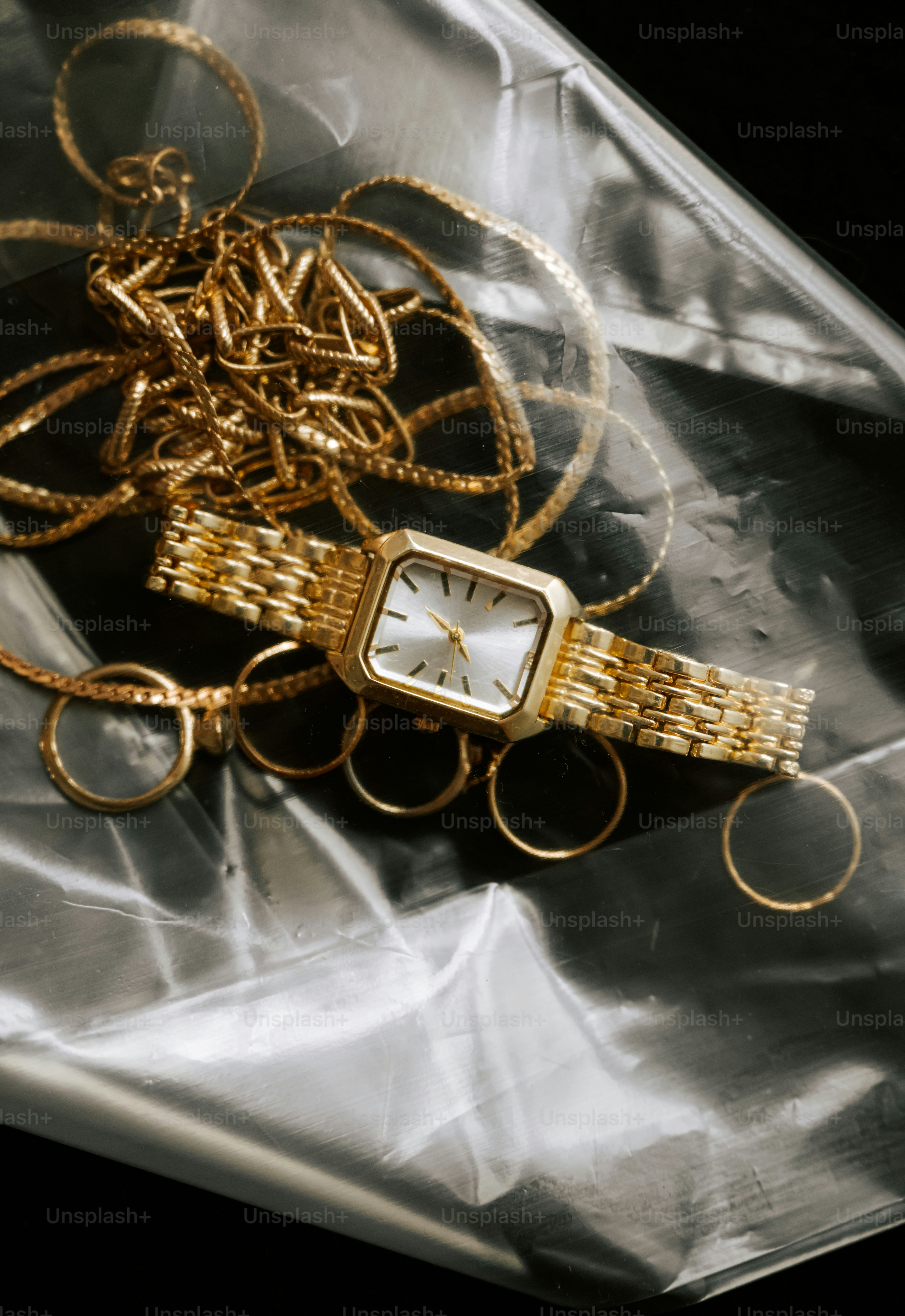 Gold watch and jewelry on plastic wrap.