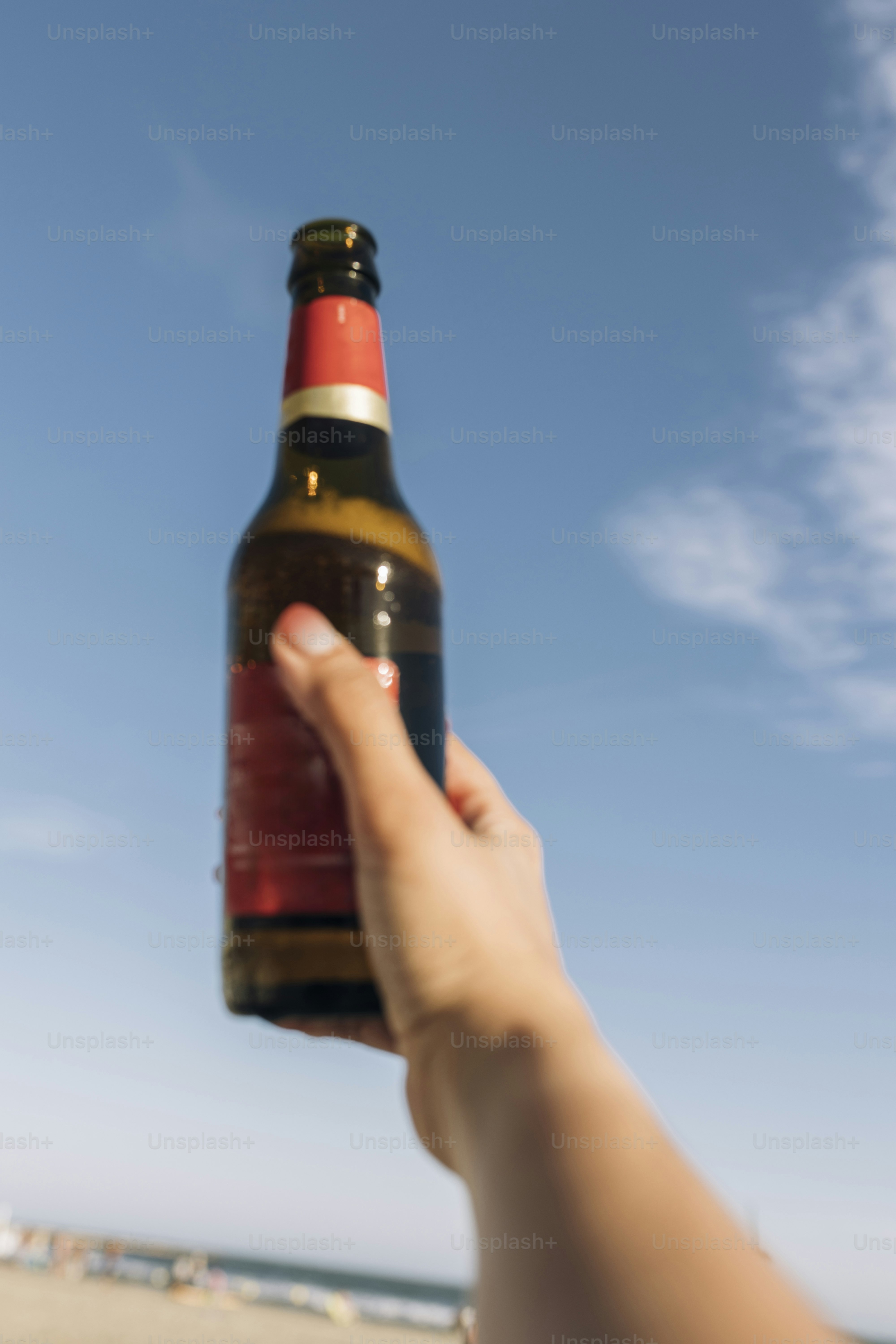 Hand holding a beer bottle against blue sky