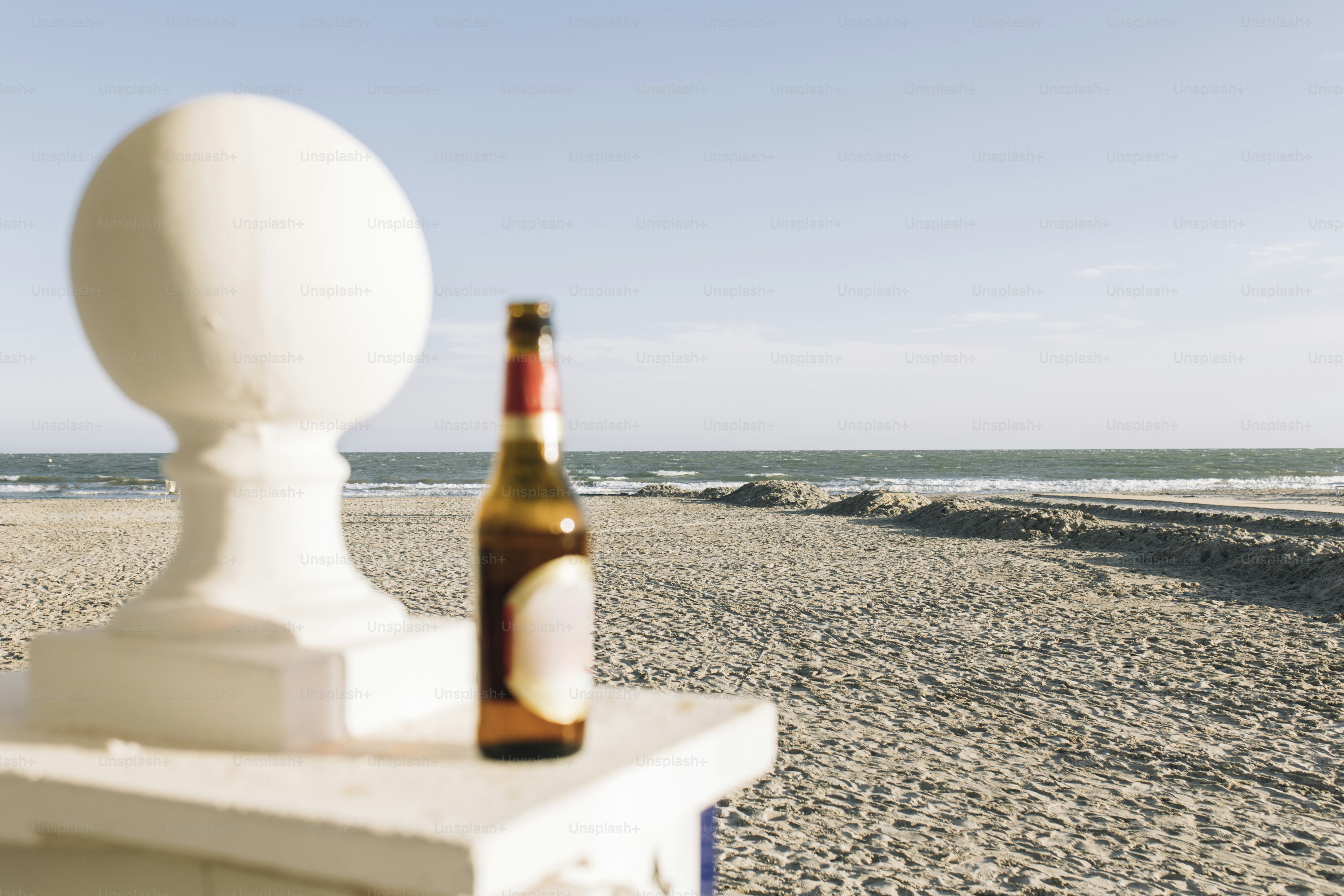 A beer bottle sits on a post at the beach.