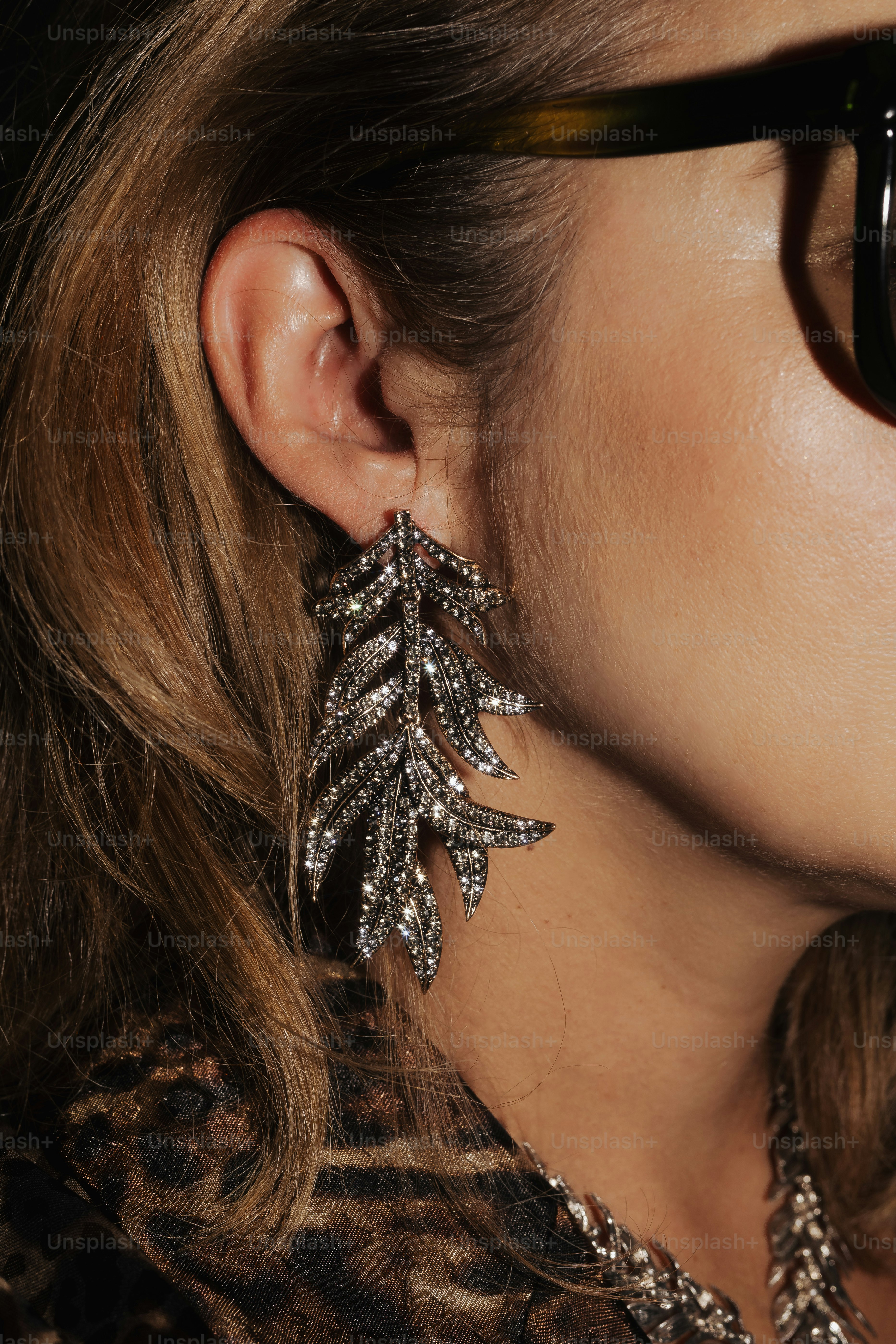 Woman wearing a large, sparkling leaf-shaped earring.