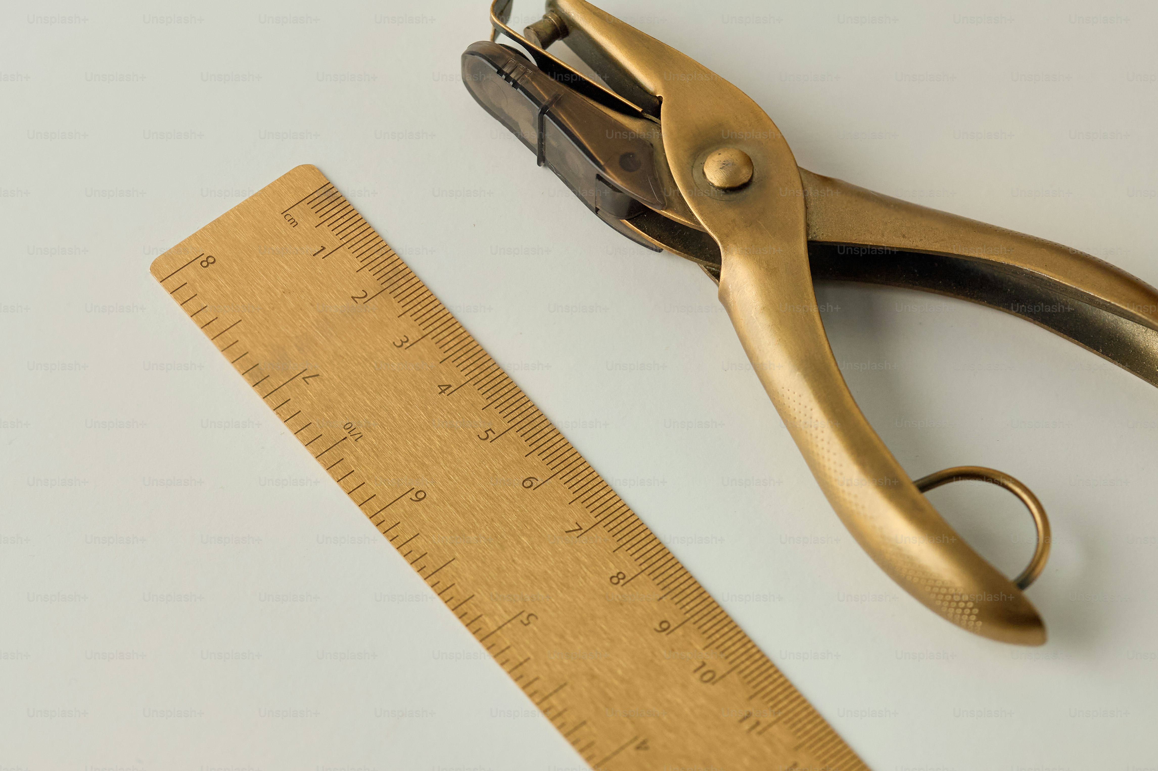 A brass hole punch and wooden ruler on white. photo – Office Image on ...