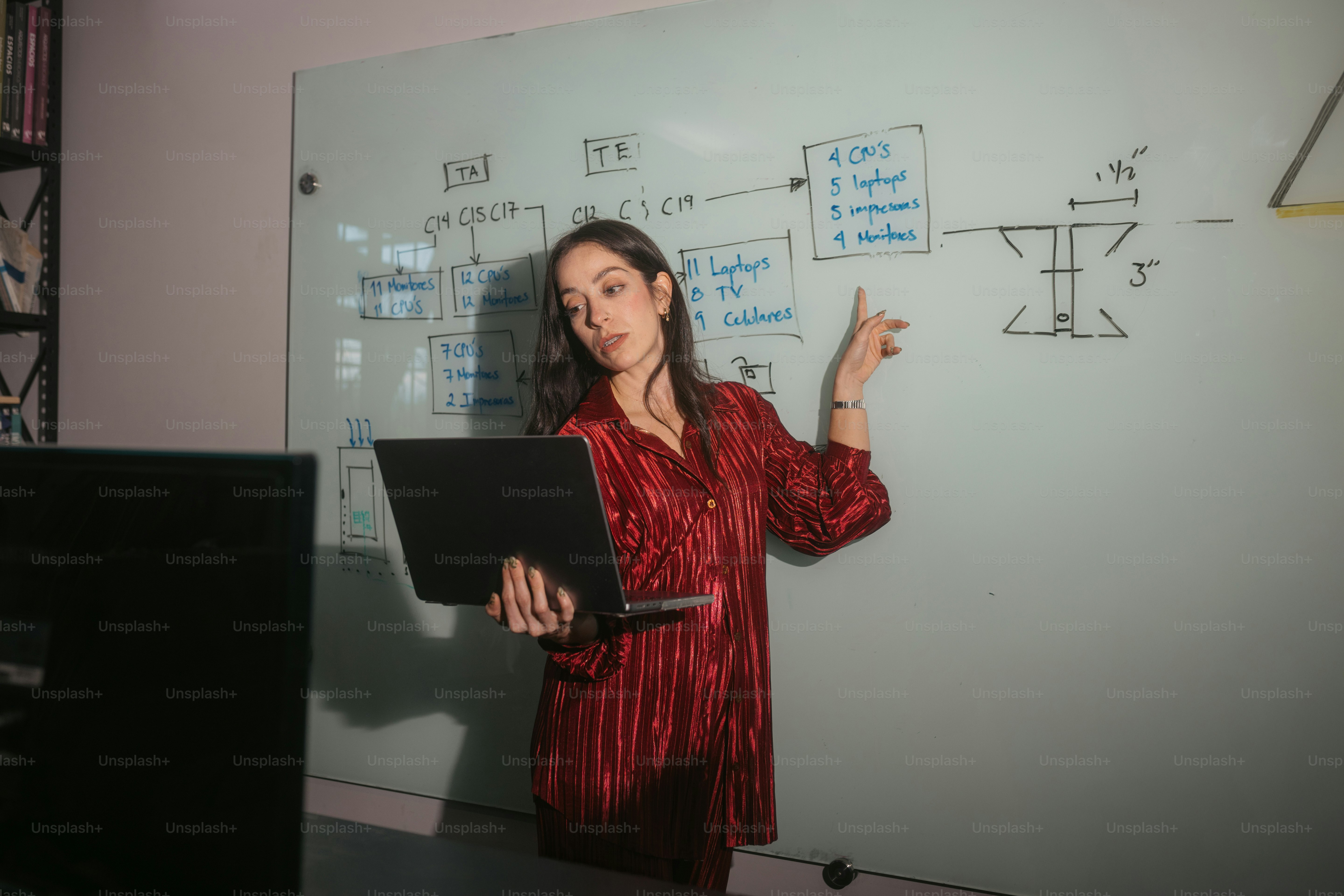 Woman holding laptop points at whiteboard diagram
