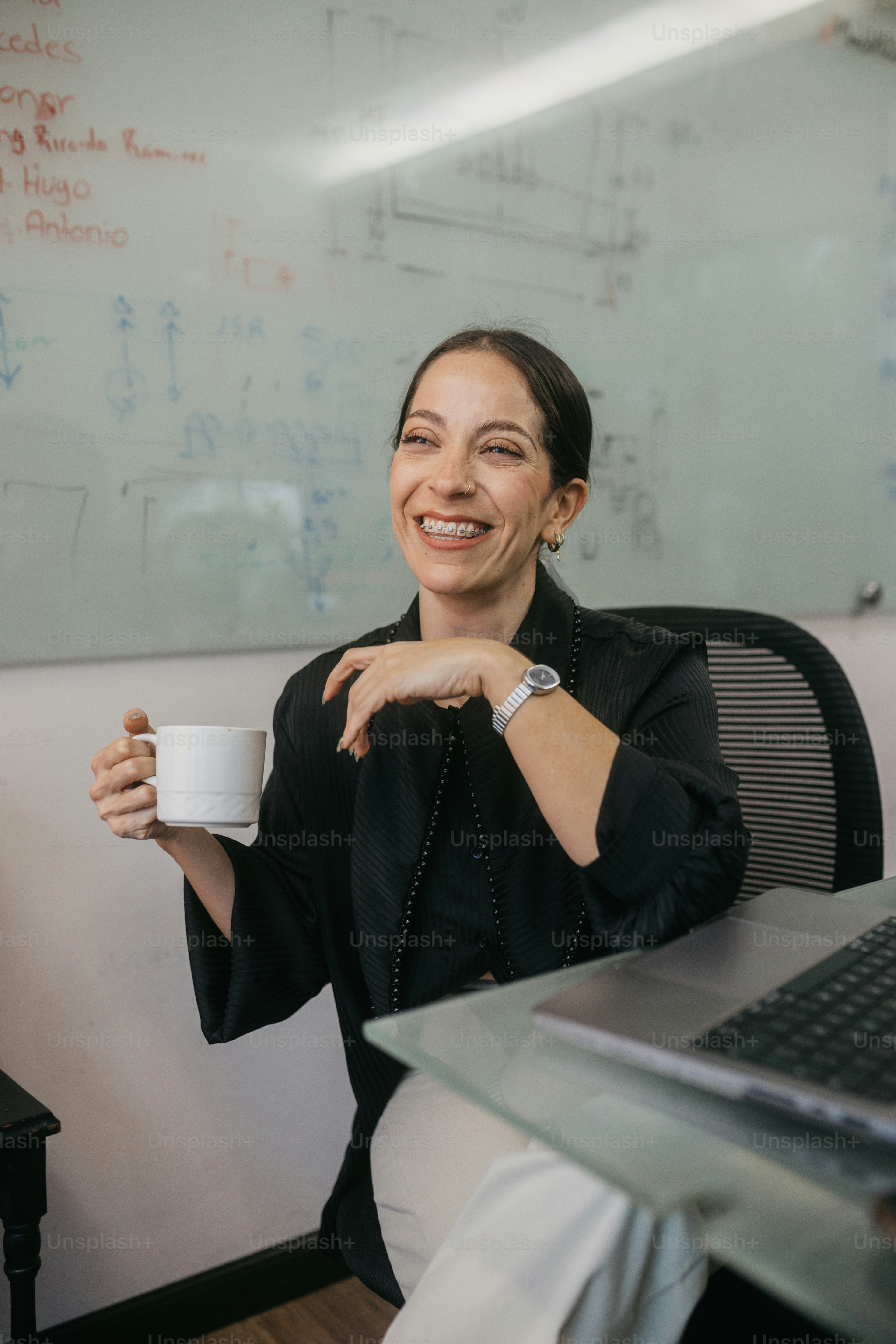 Woman holding coffee cup, laughing in office meeting