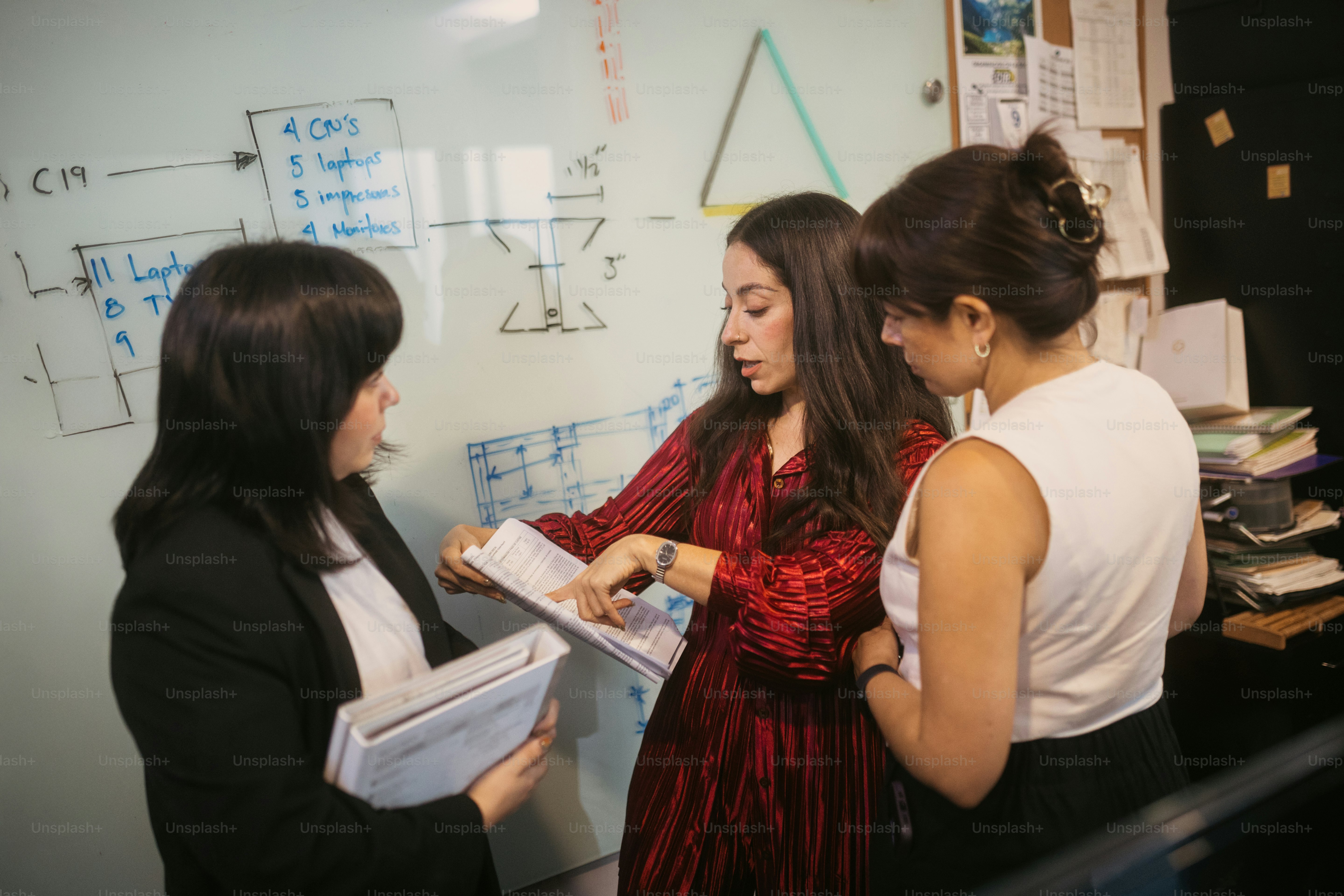 Three women collaborating near a whiteboard with diagrams