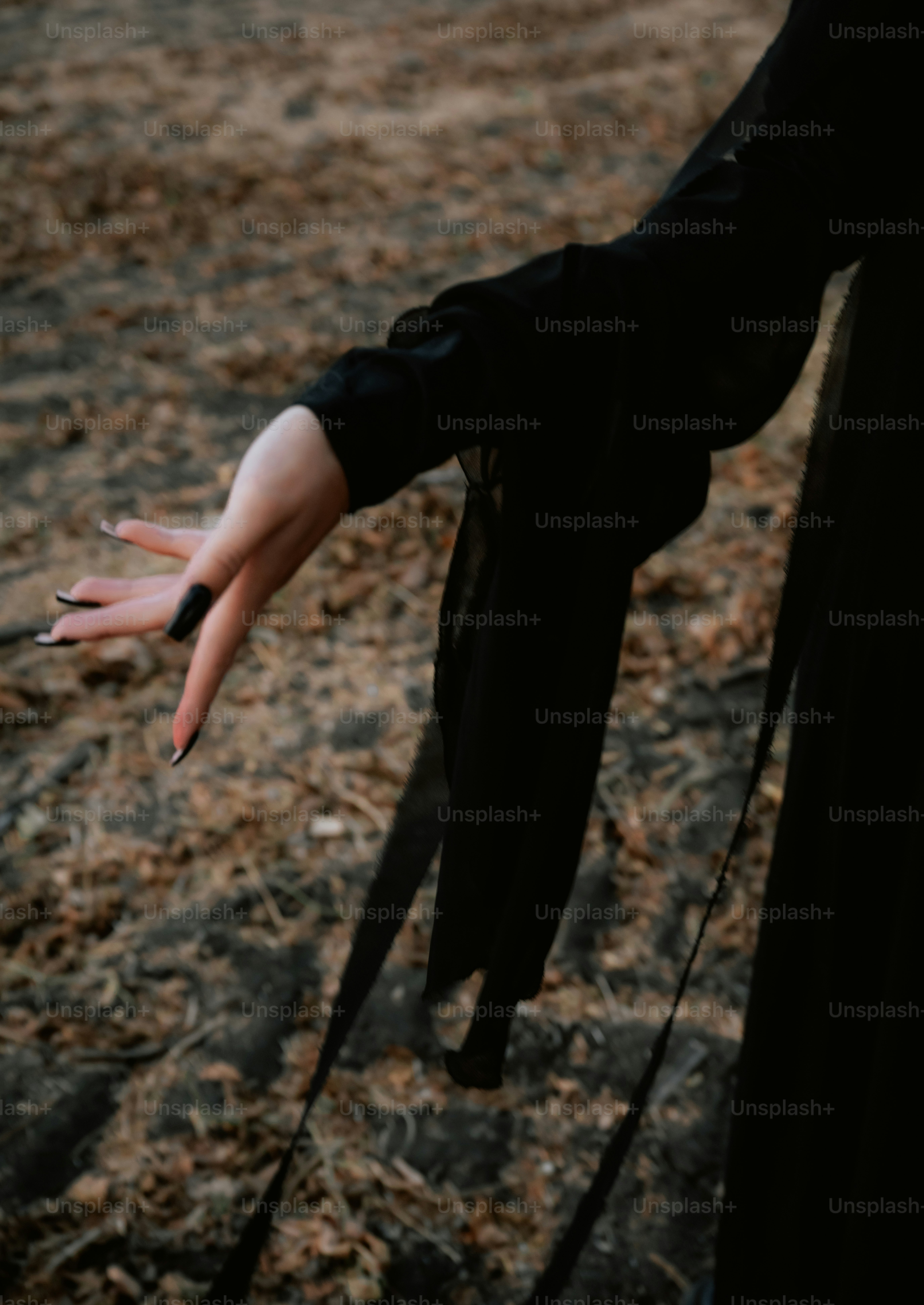 A hand with black nails reaches out in darkness.
