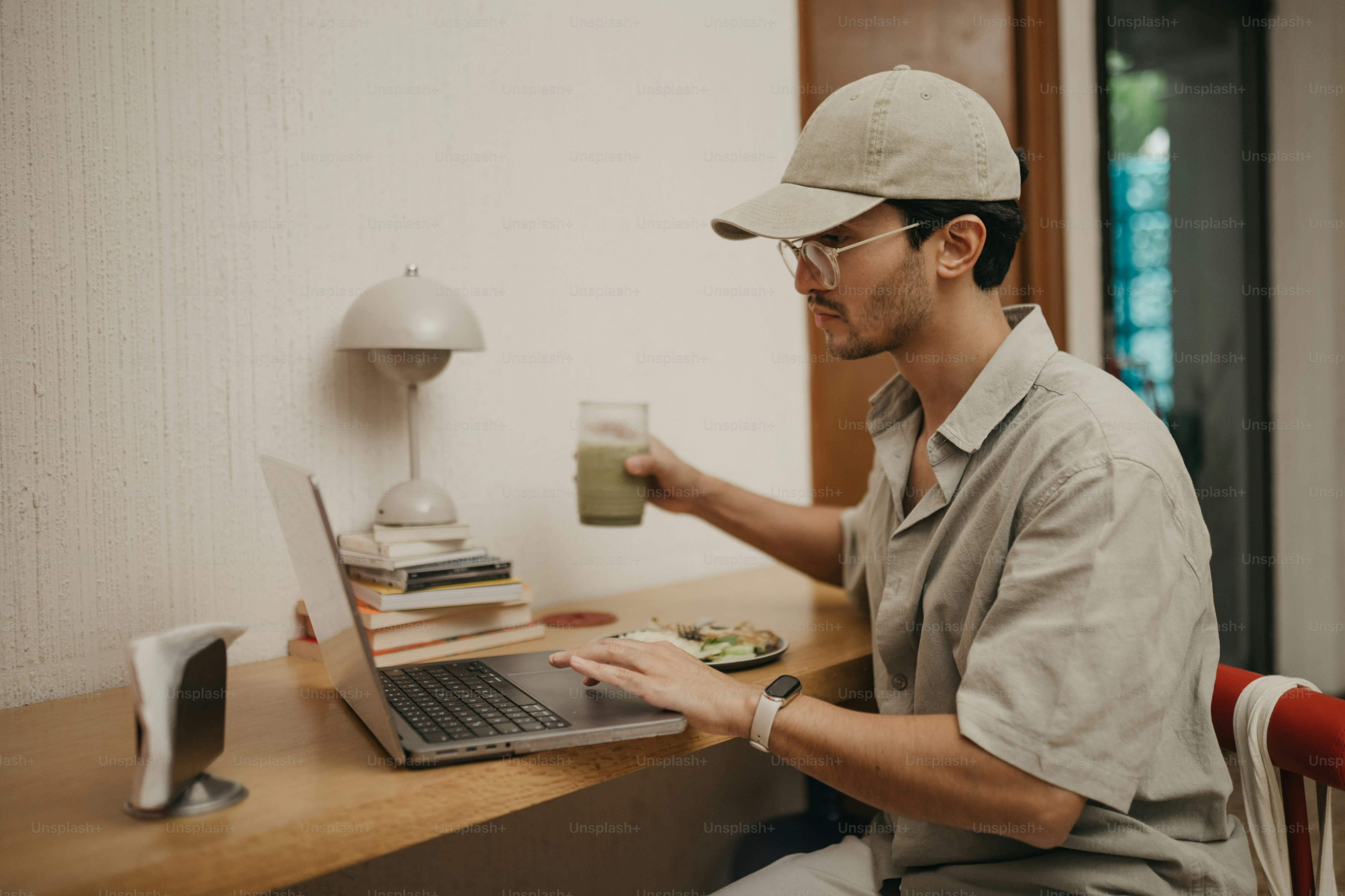 Man in hat drinks green beverage while using laptop