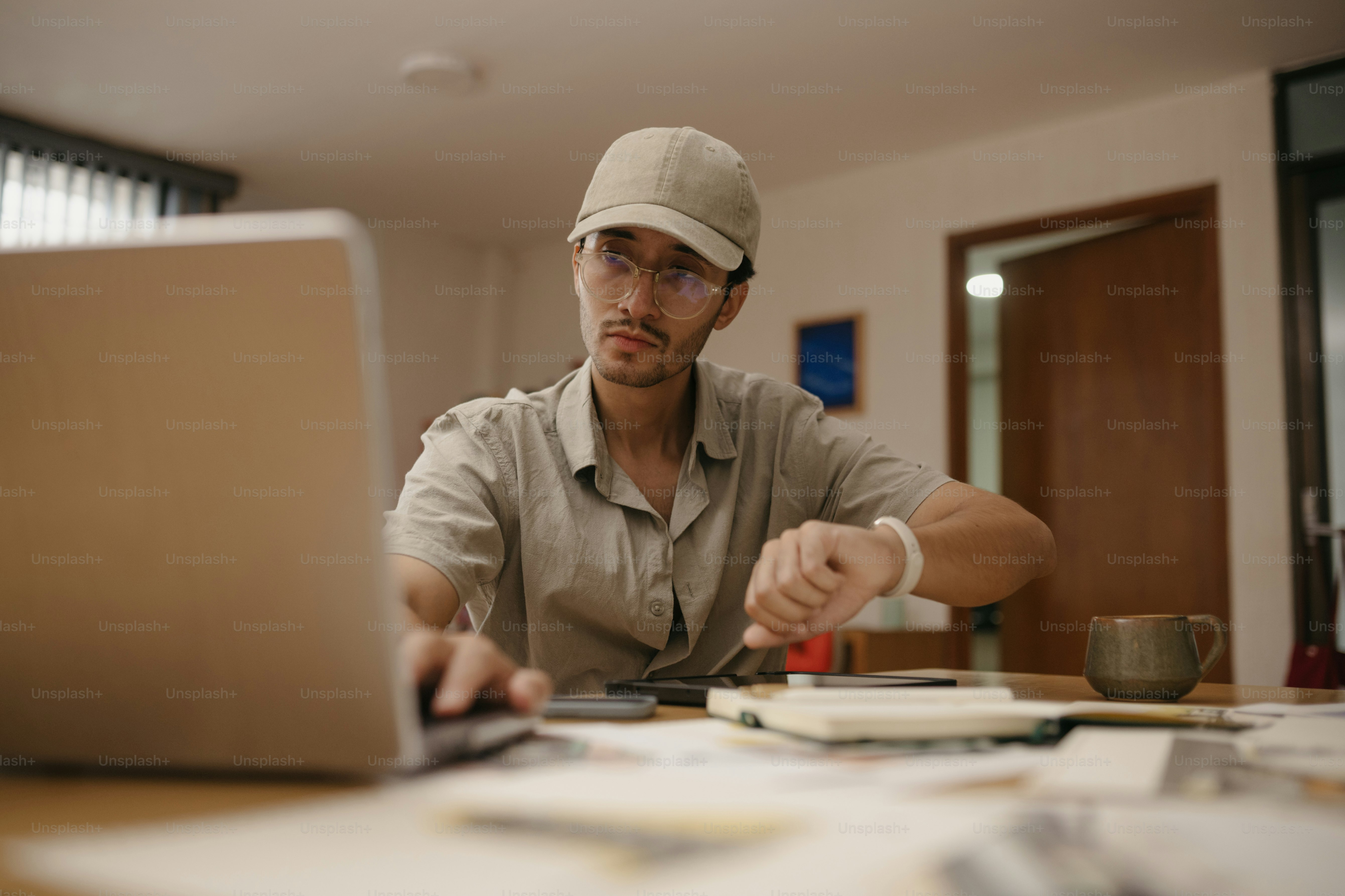 L'uomo con berretto da baseball controlla l'orologio mentre lavora sul laptop.