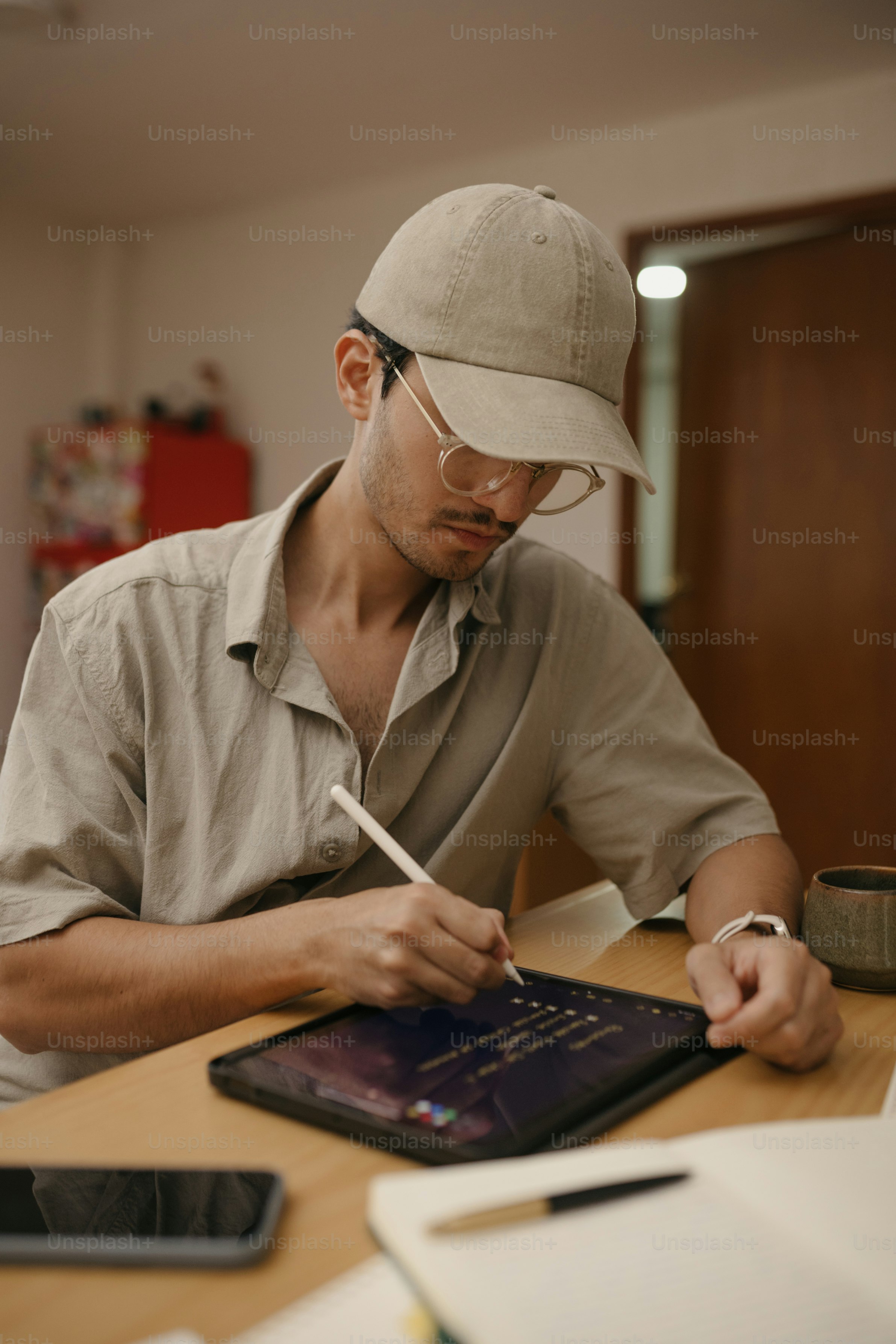 Man wearing glasses and cap drawing on tablet