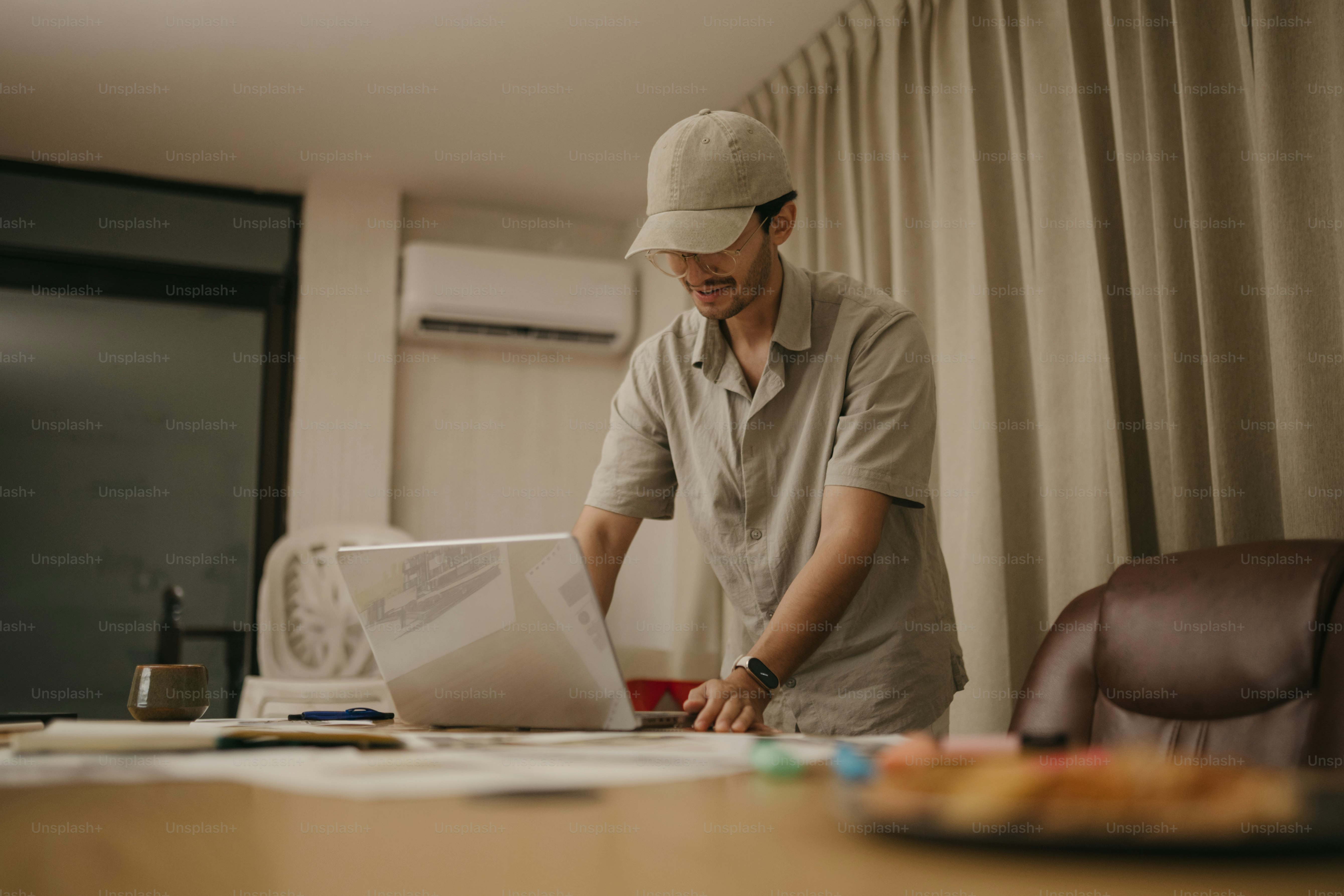 Man in baseball cap working on laptop at desk.