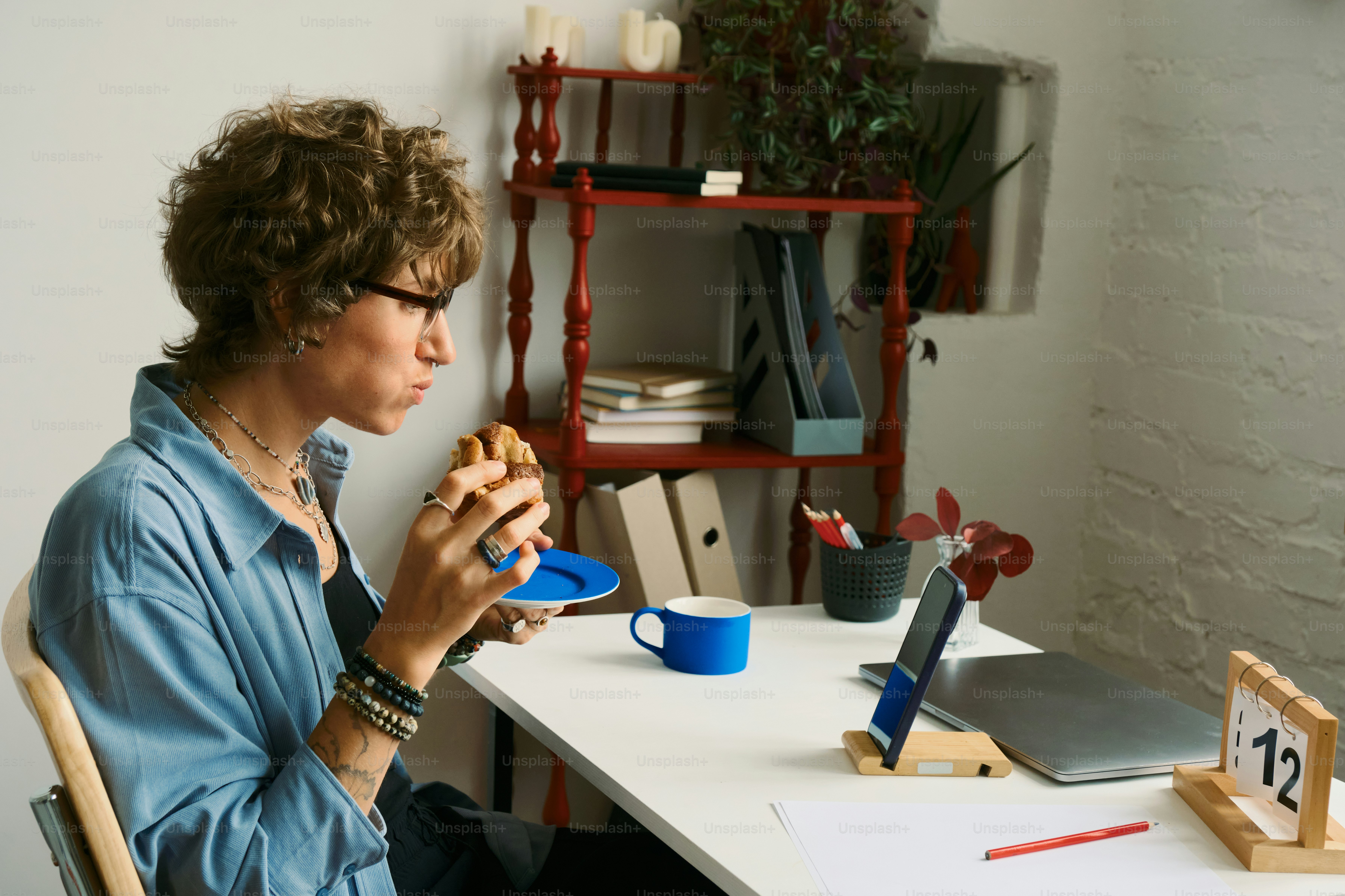 Woman eating a sandwich at a desk with laptop.