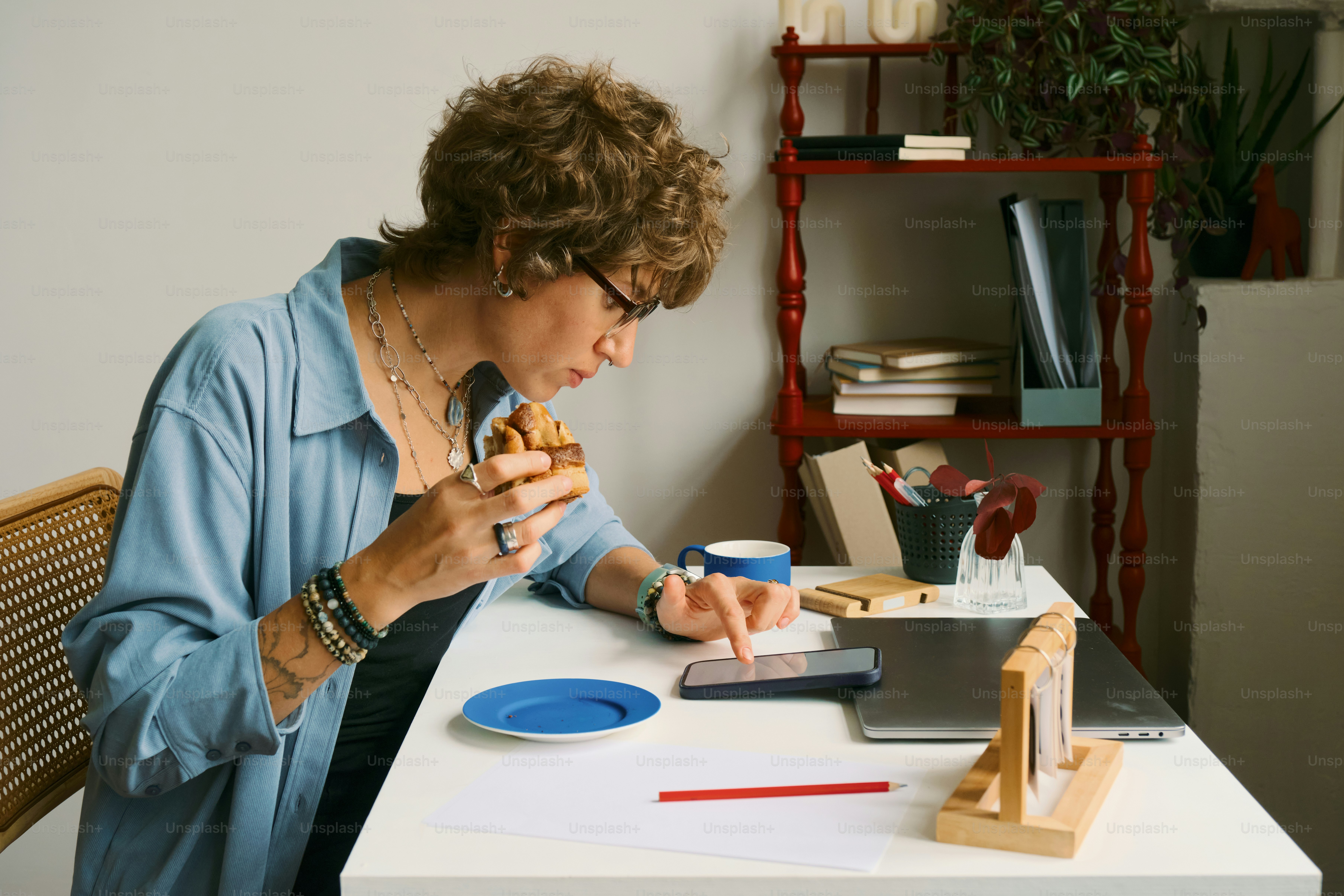 Woman eating a pastry while looking at her phone.