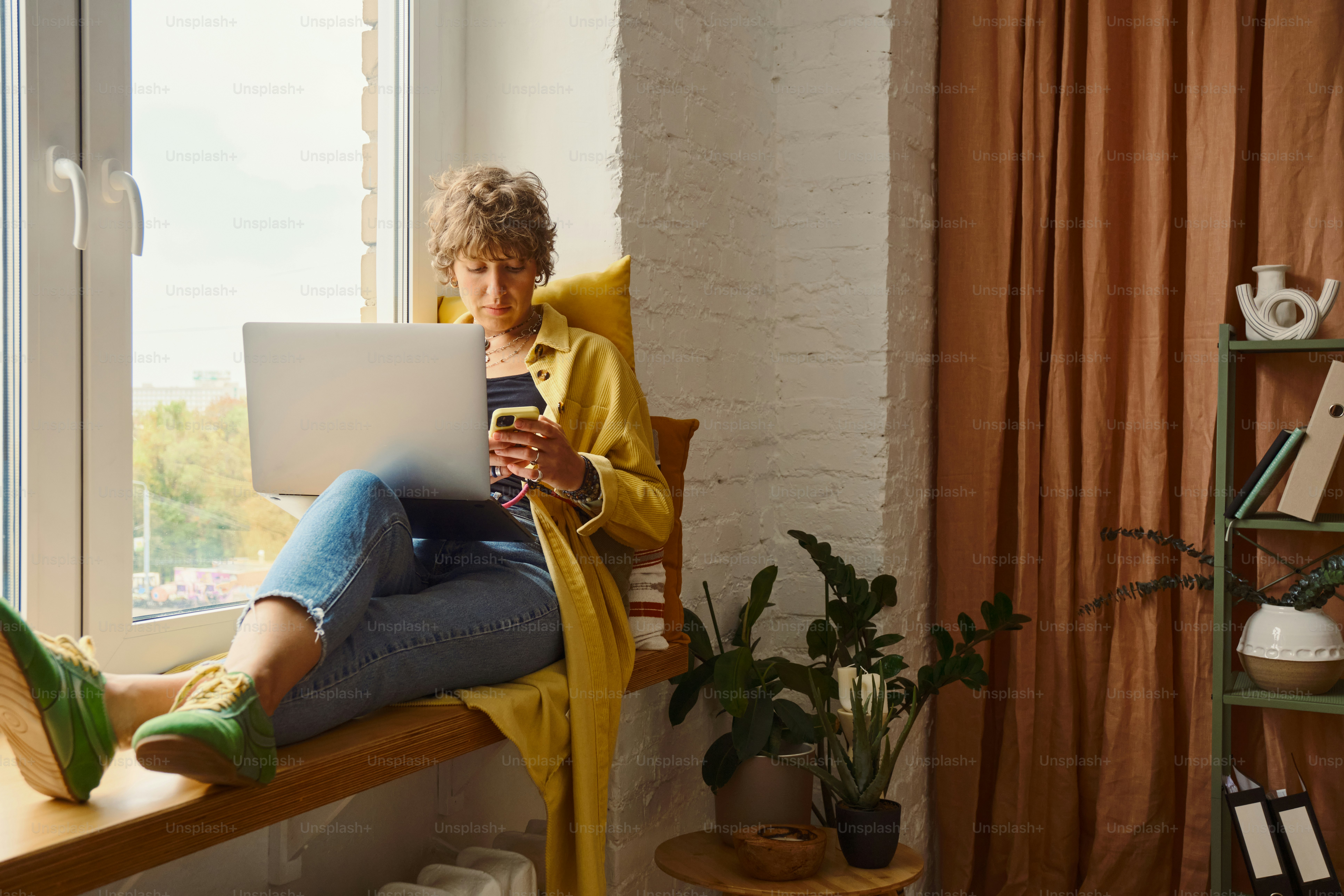 Mulher que trabalha no portátil pela janela ensolarada