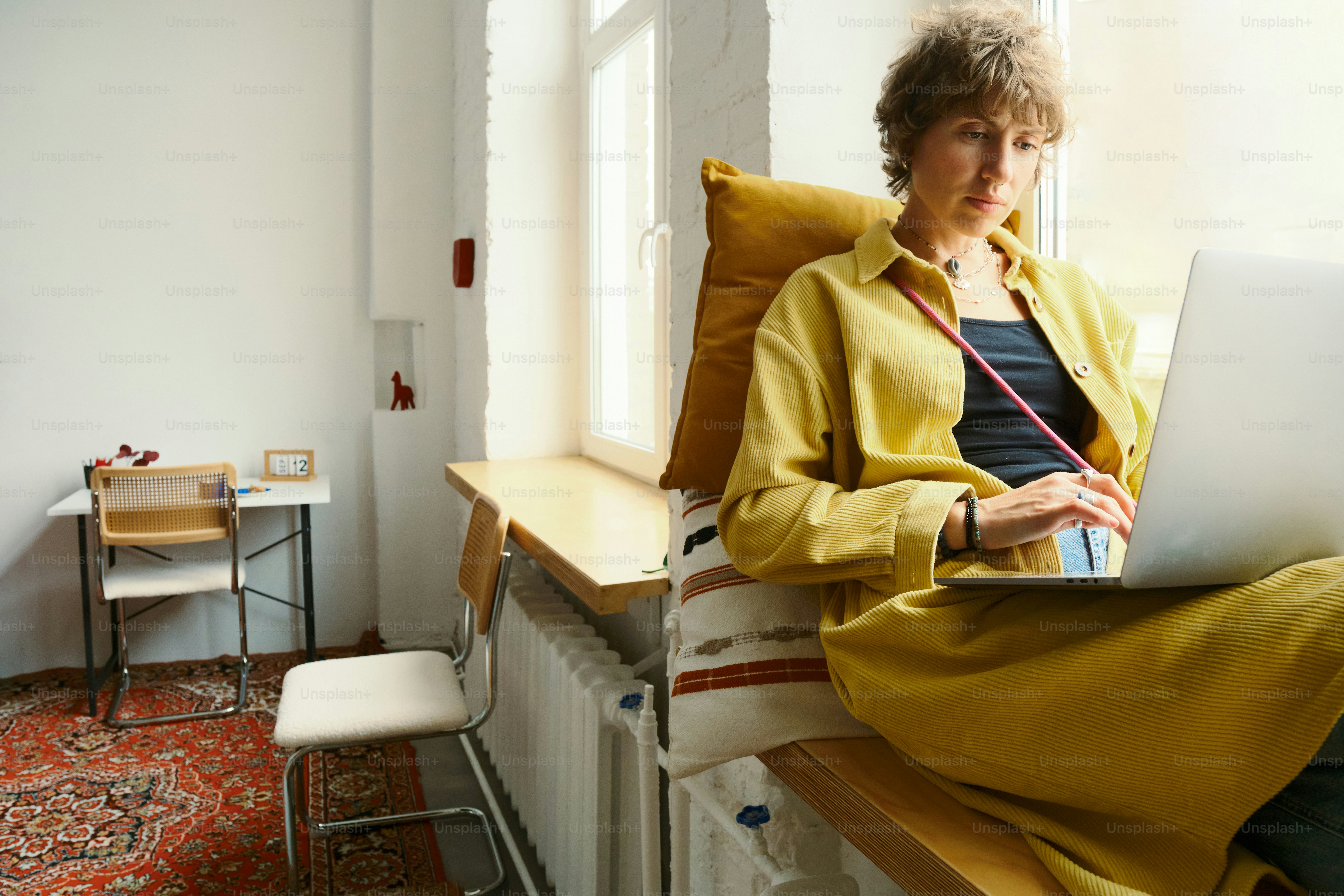 Mulher que trabalha no portátil pela janela