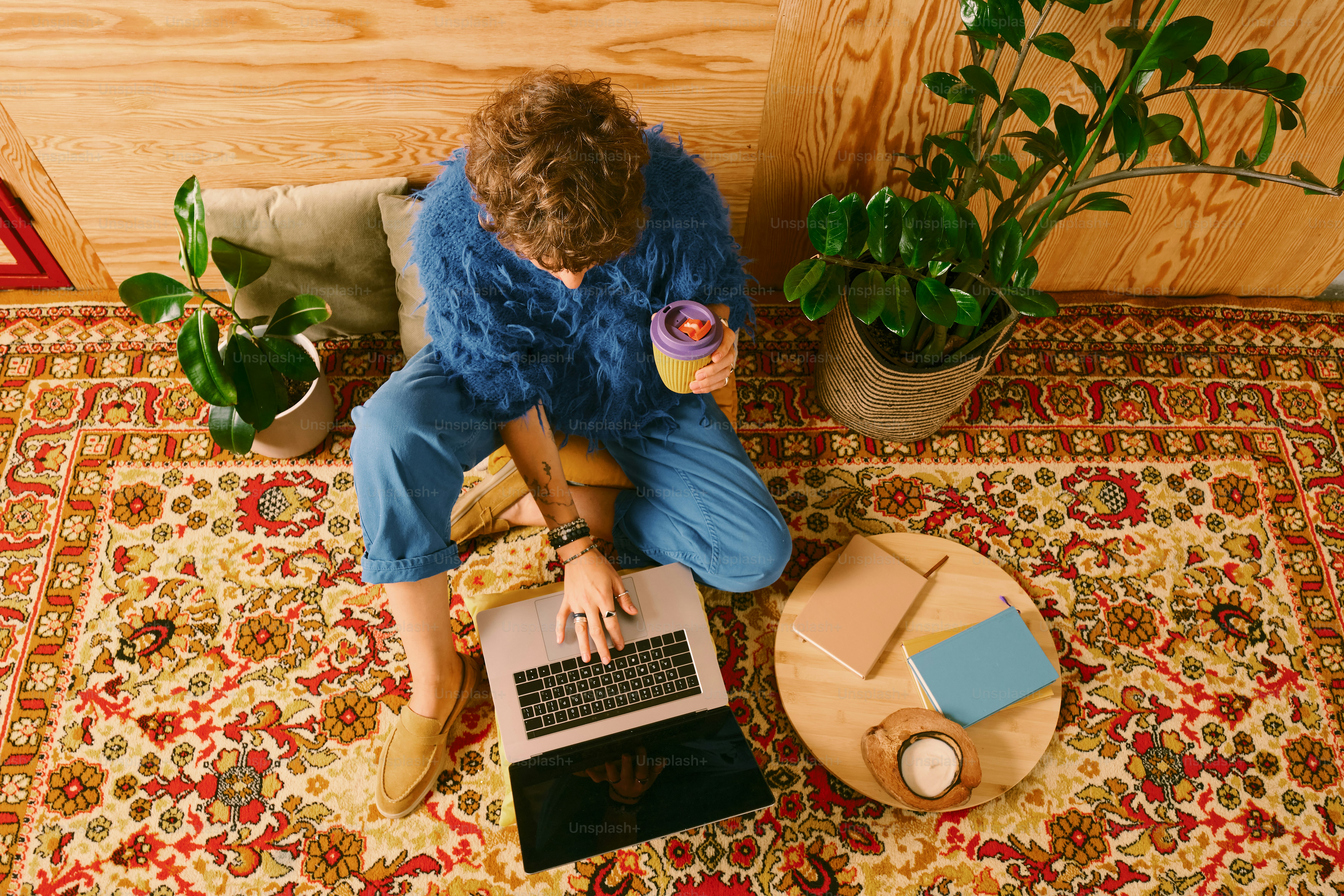Mulher trabalhando no laptop com café no tapete ornamentado.
