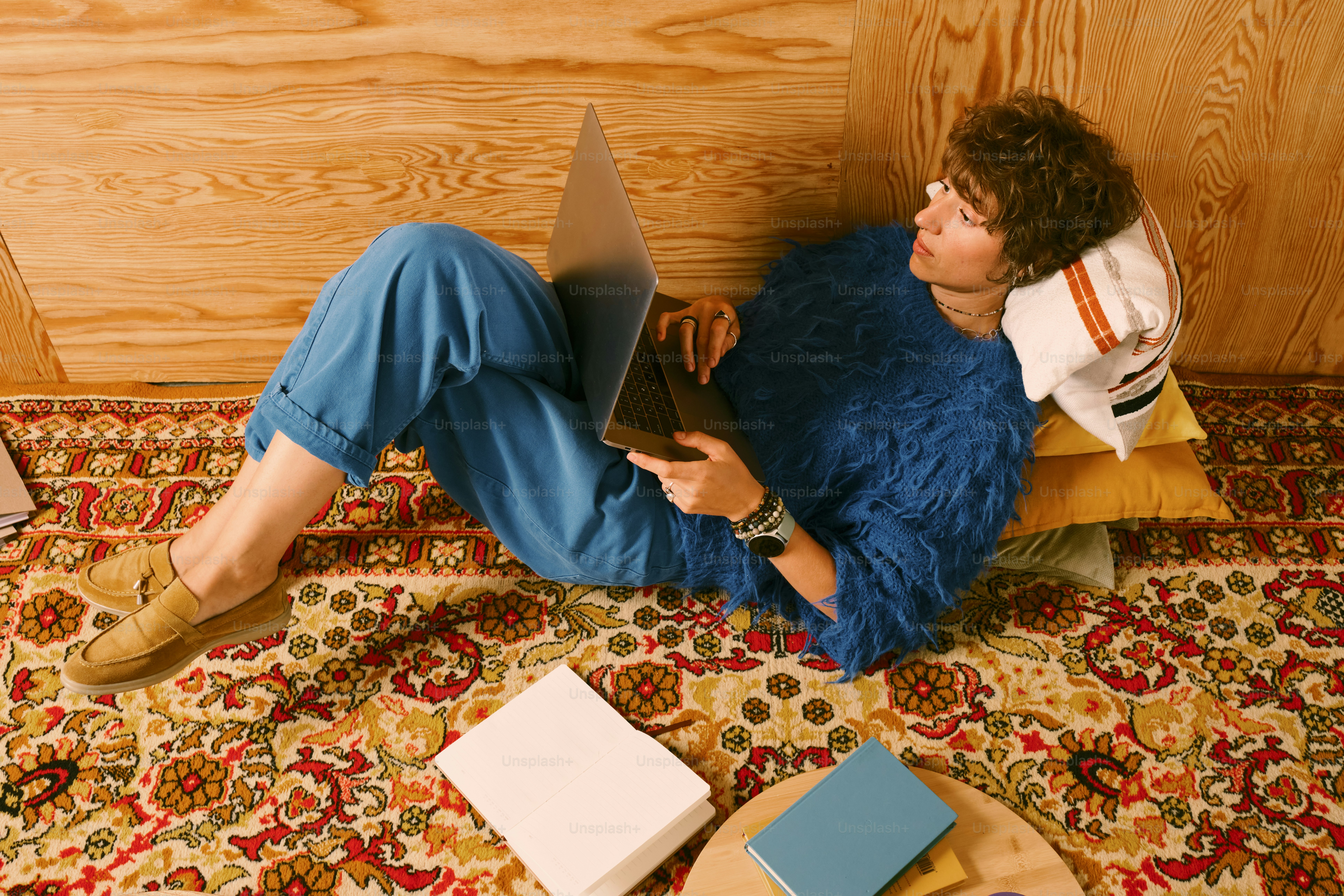 Mulher de camisola azul trabalha no laptop no tapete.