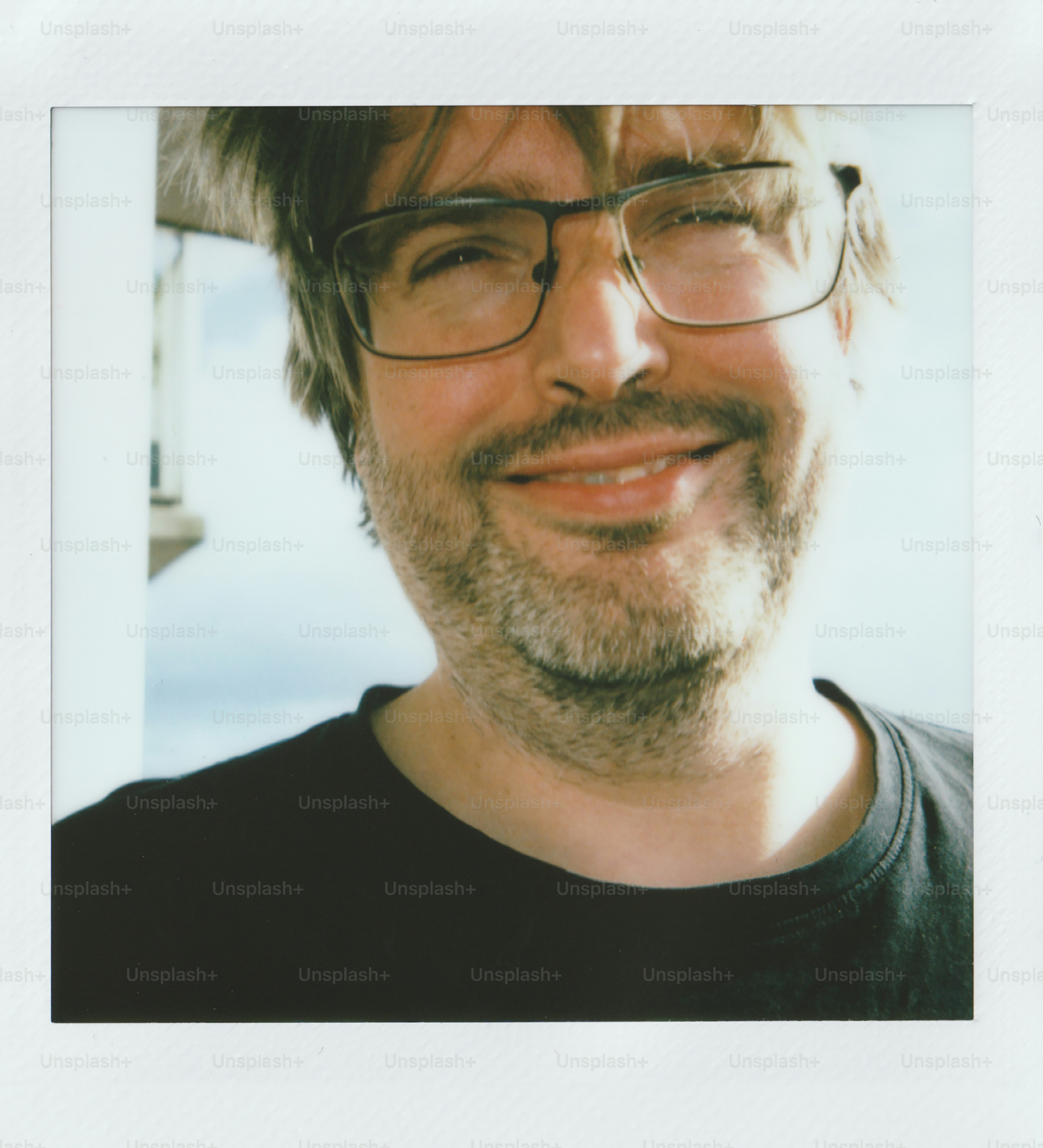 A smiling man with glasses wearing a dark t-shirt.