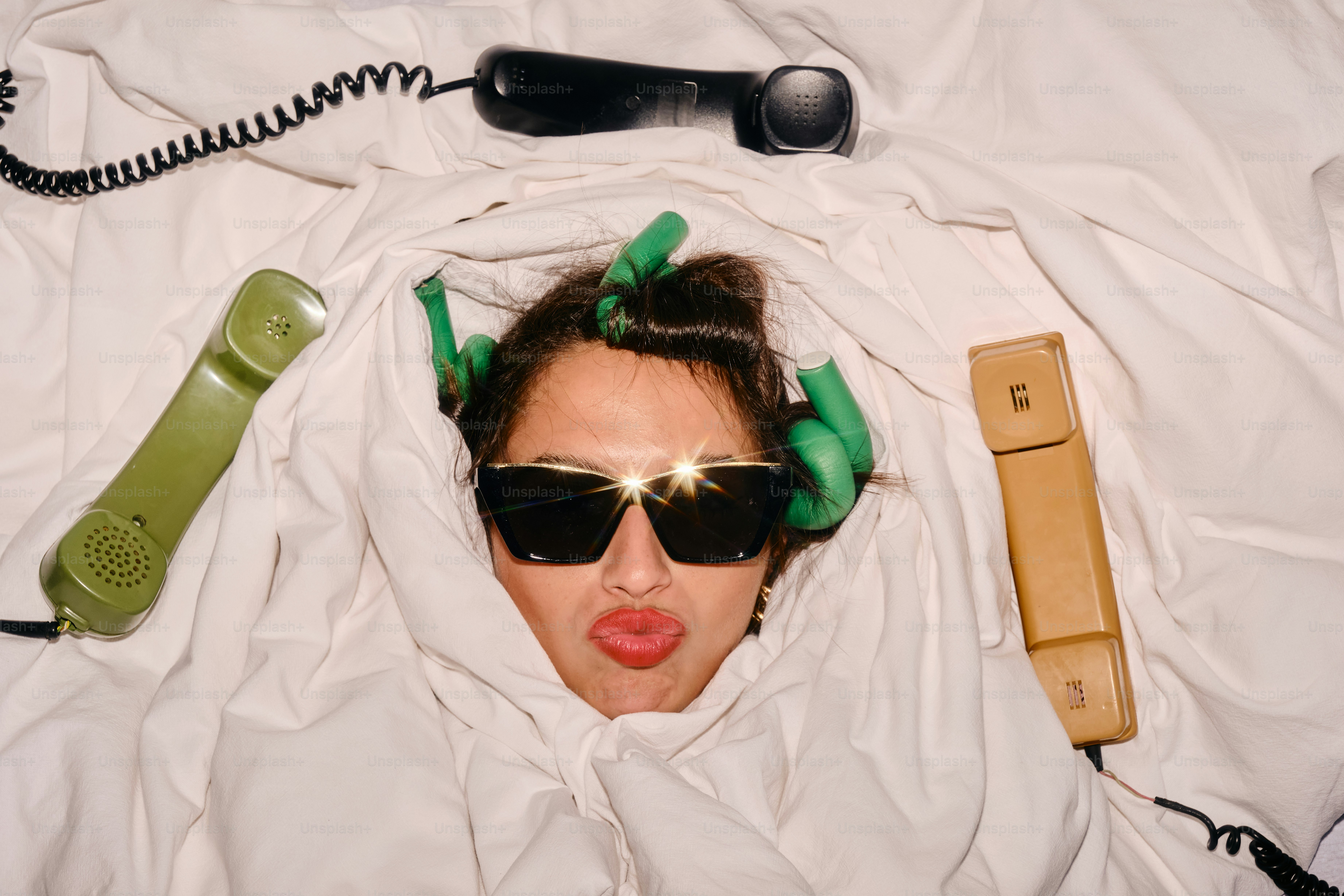 Mujer en la cama con rulos, gafas de sol y teléfonos
