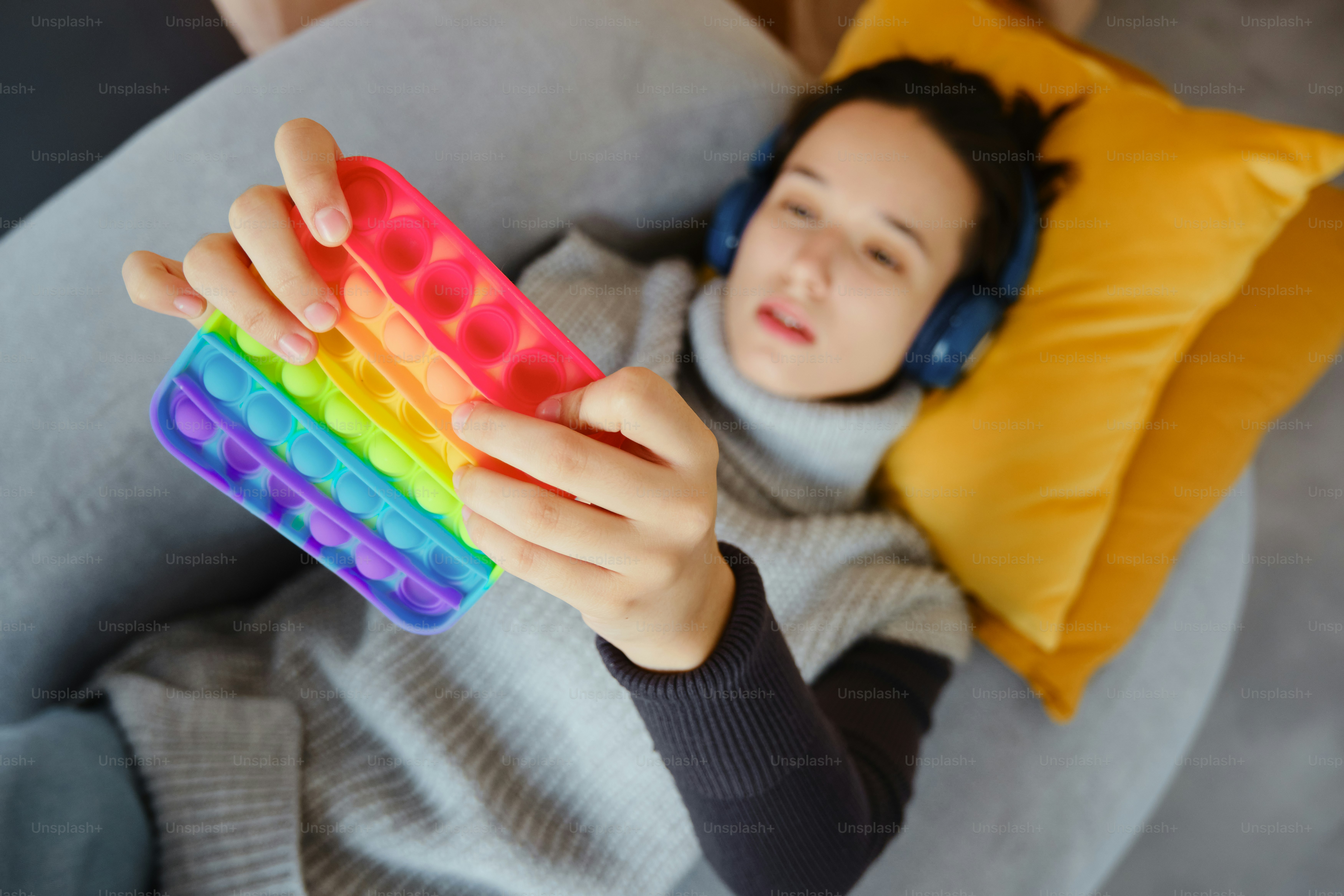 Wanita muda dengan headphone bermain dengan mainan gelisah berwarna-warni.