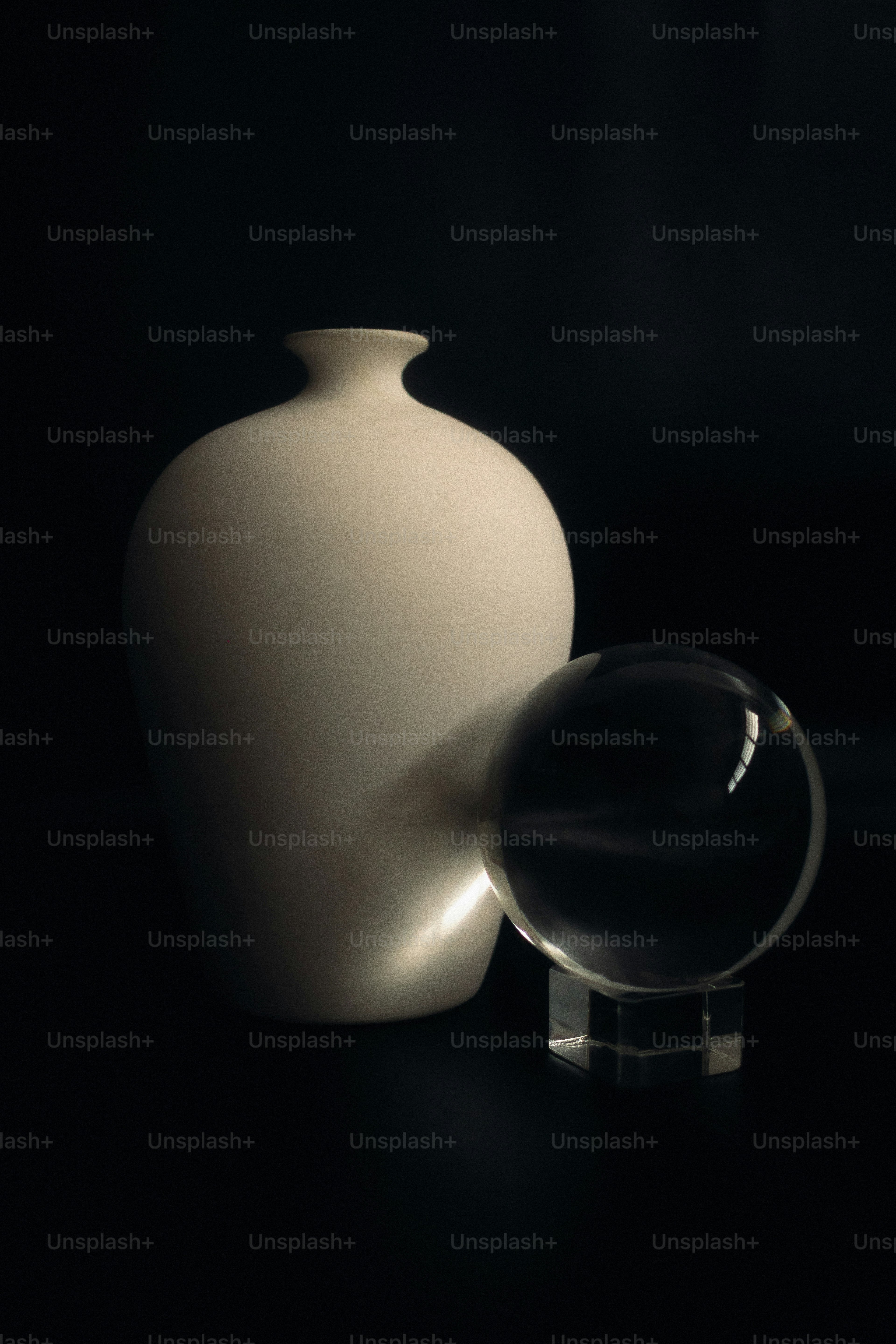 A white vase and glass sphere on dark background