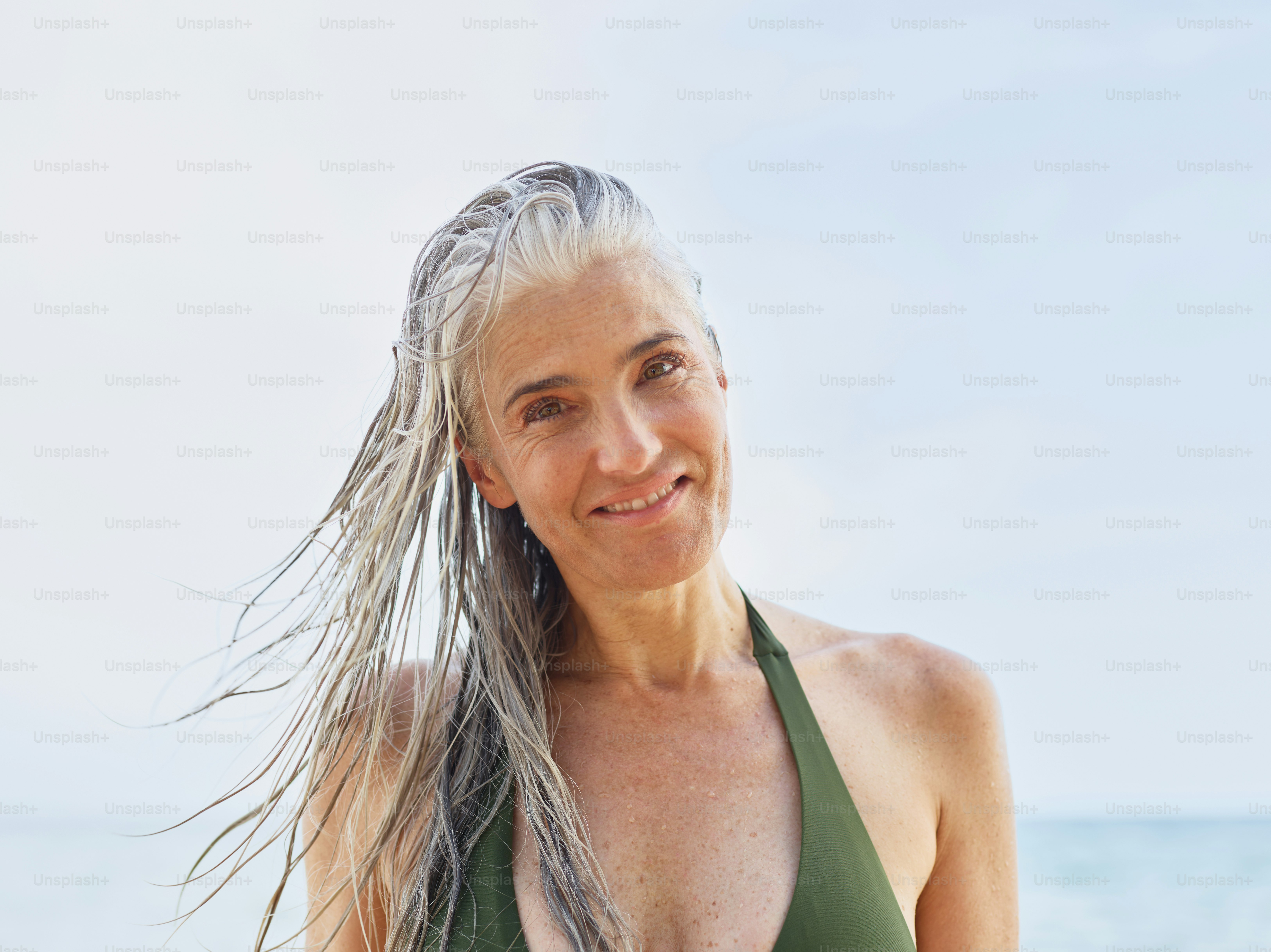 A smiling woman with long gray hair at the beach.