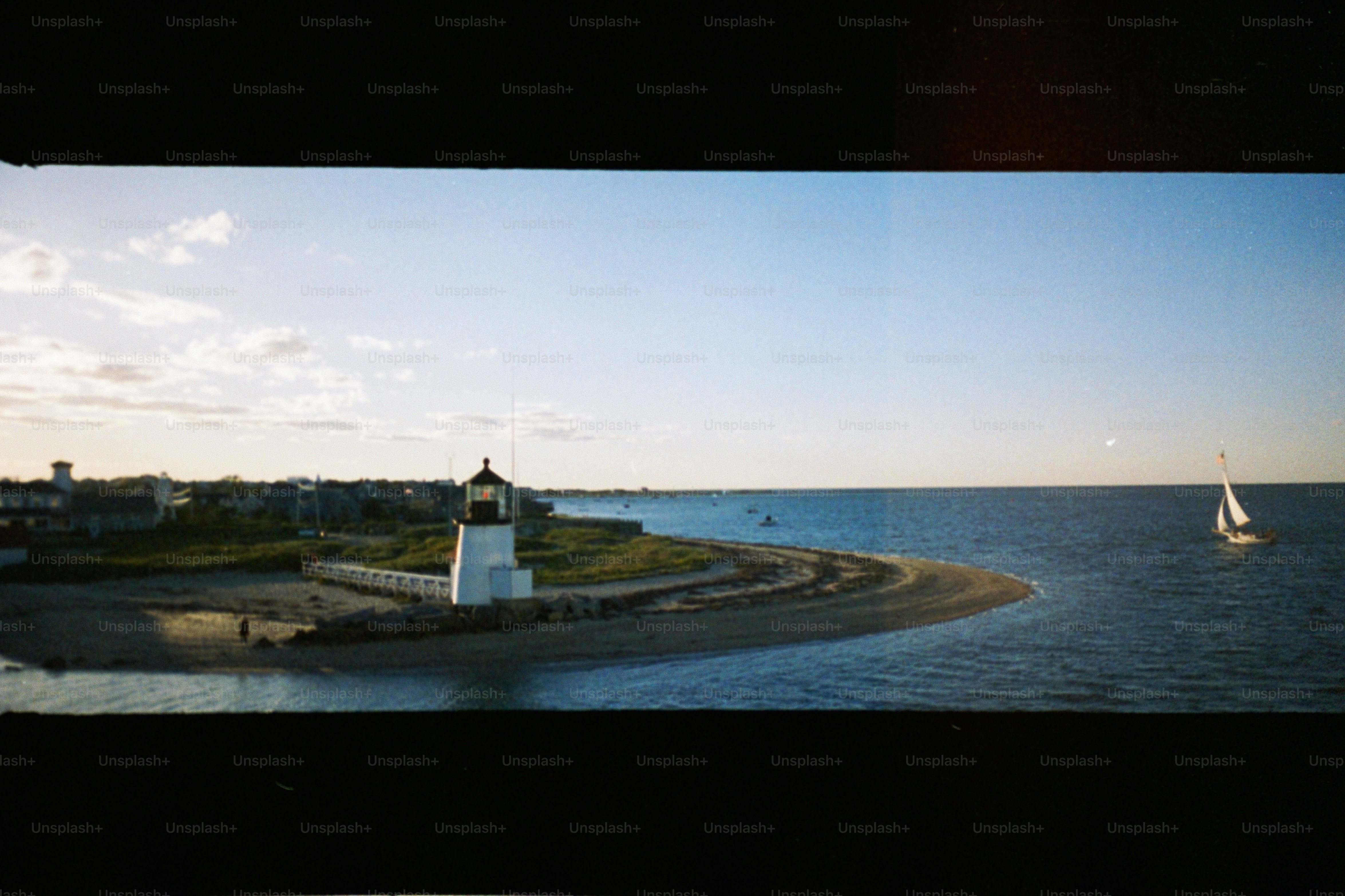 Lighthouse on a peninsula with a sailboat nearby.