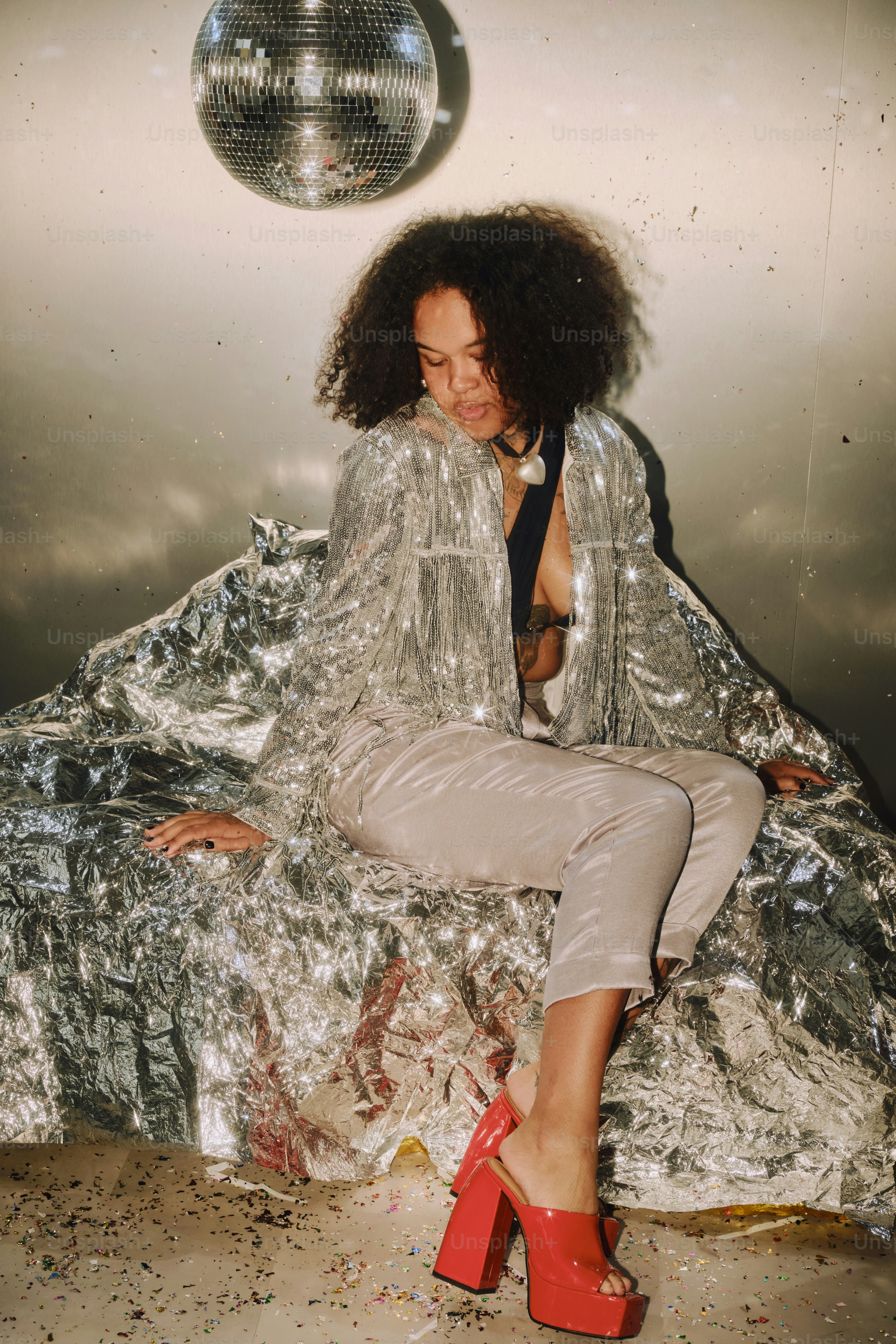 Woman in sparkly outfit sits near disco ball.
