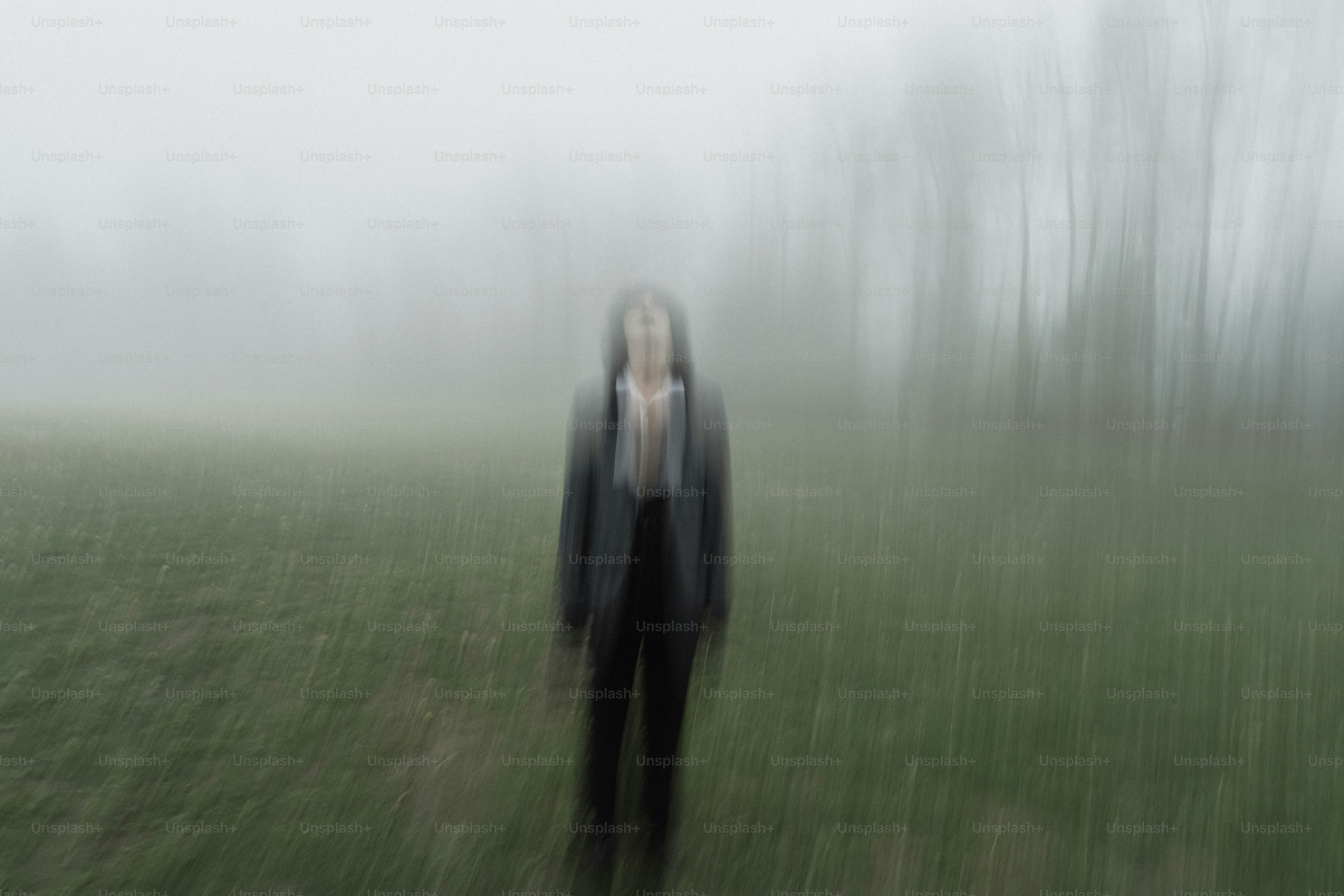 Person in a suit stands in foggy field with trees.