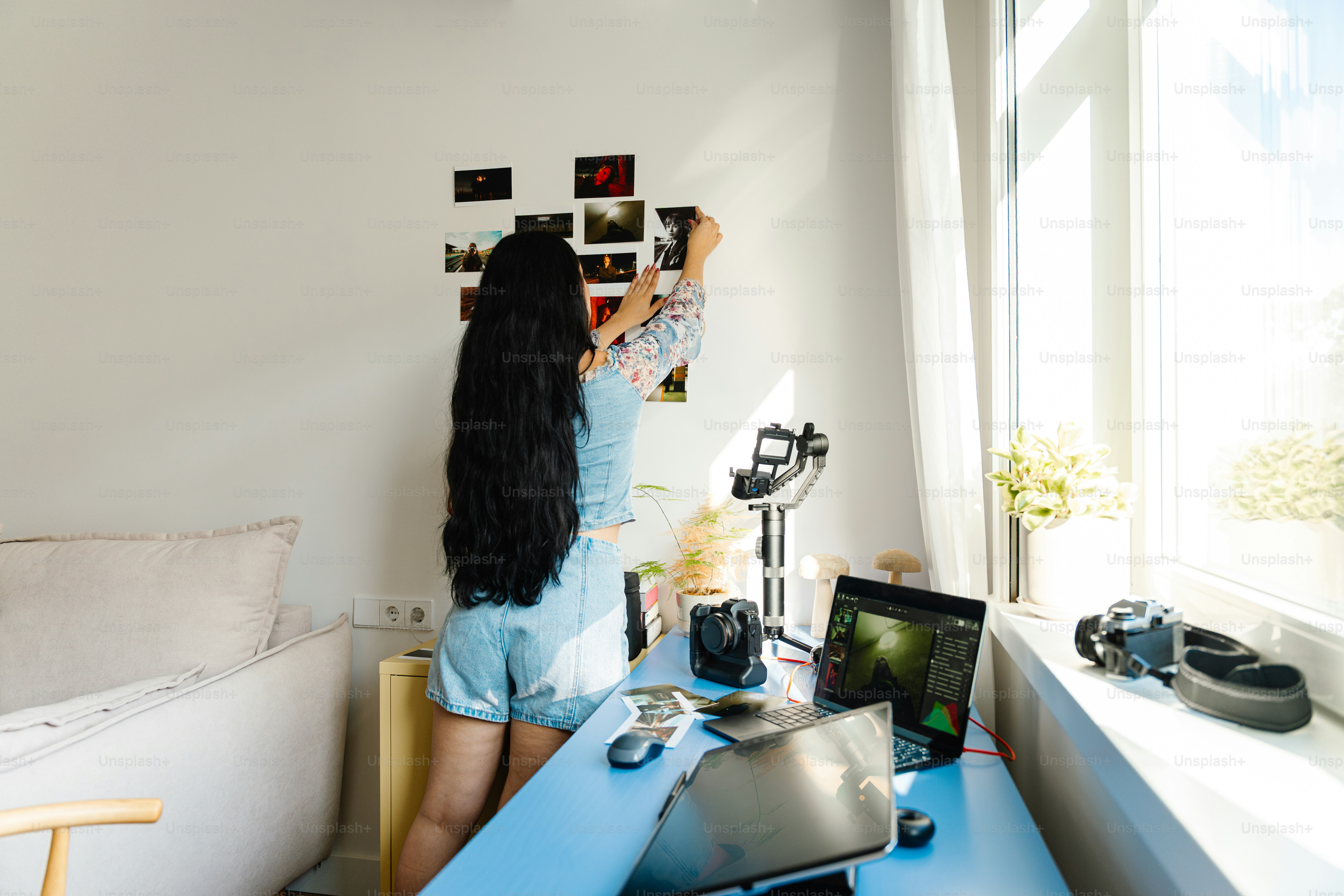 Woman hangs photos on wall above desk.