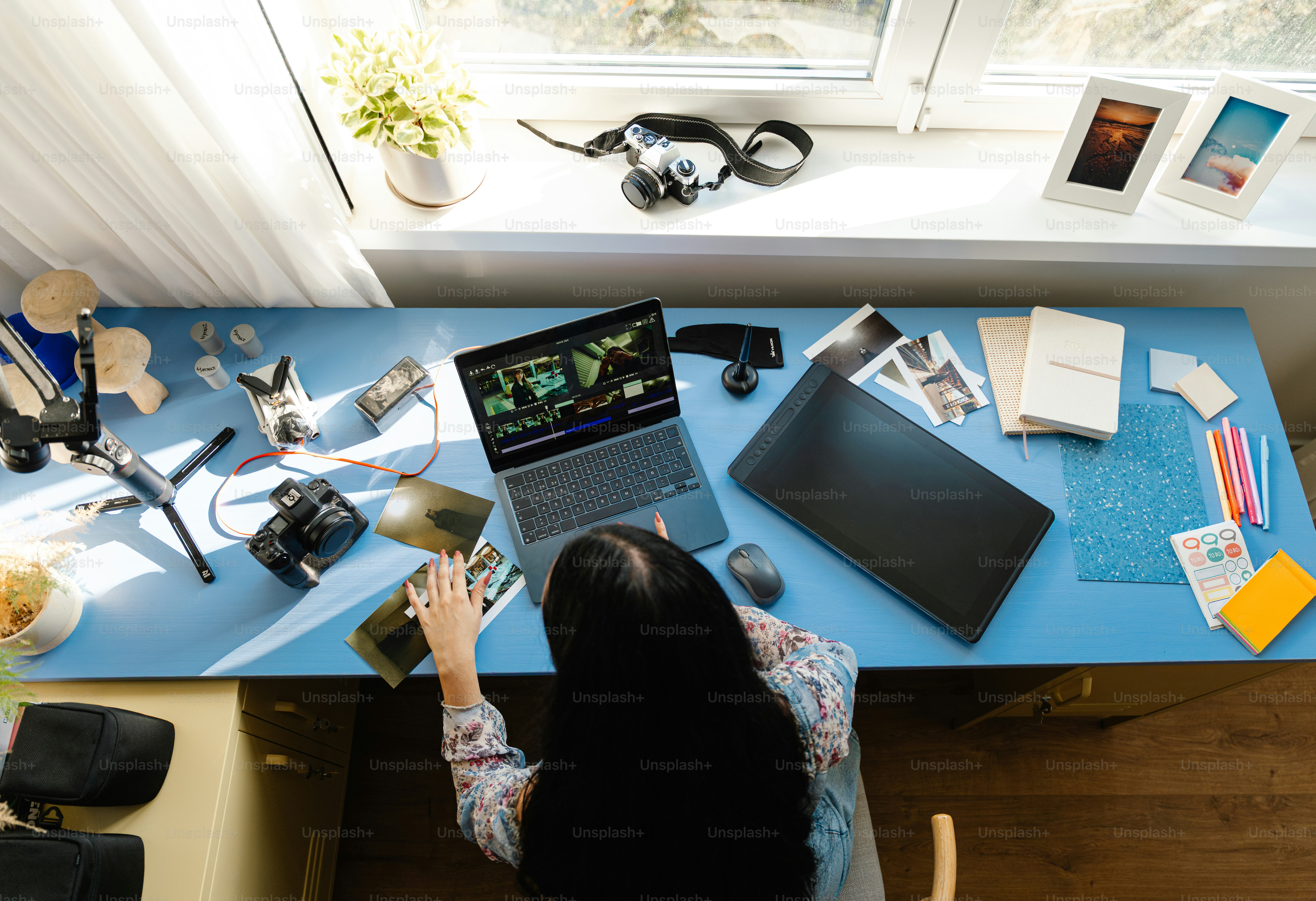 Person working at a cluttered desk with camera equipment.