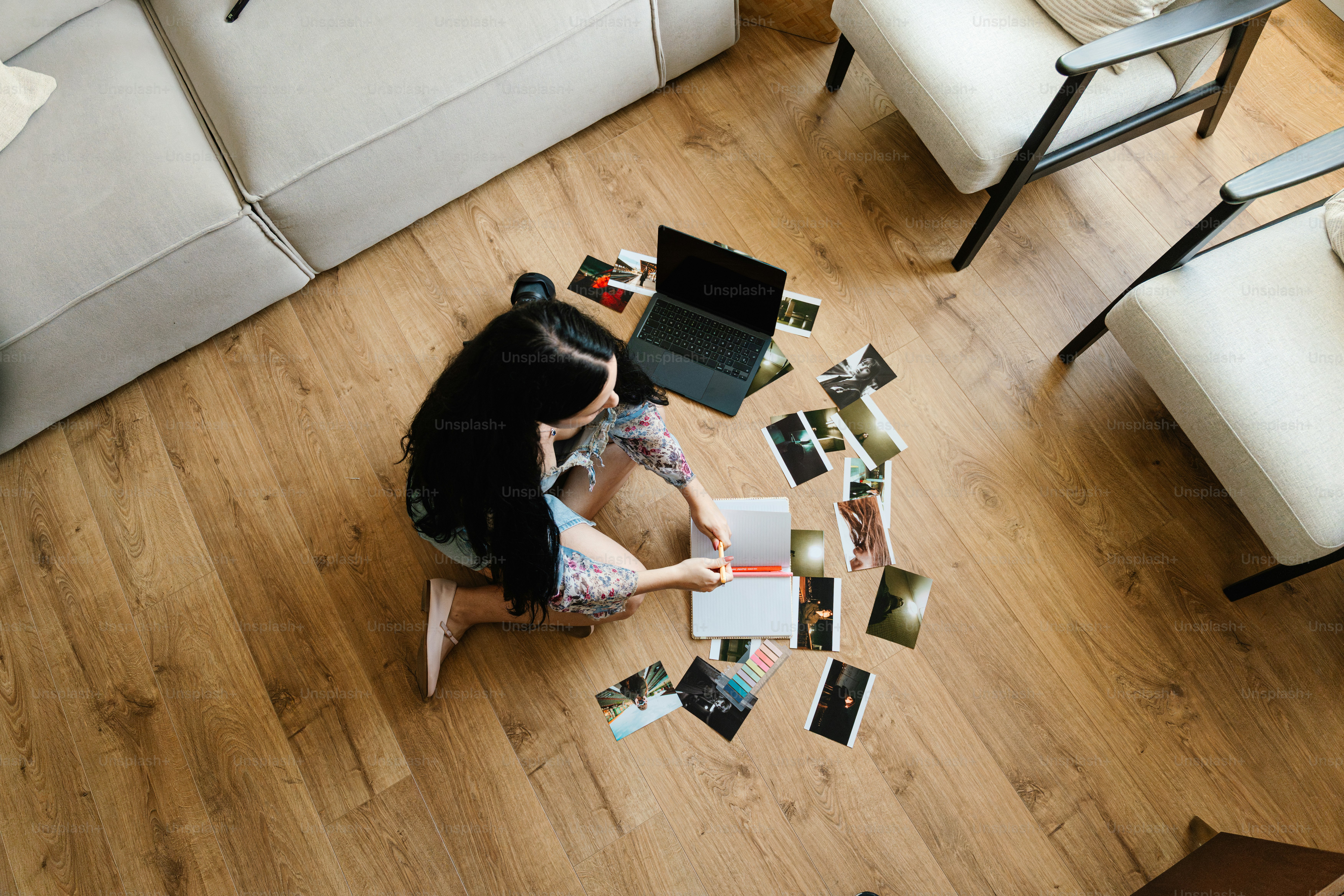 Woman surrounded by photos and laptop on floor.
