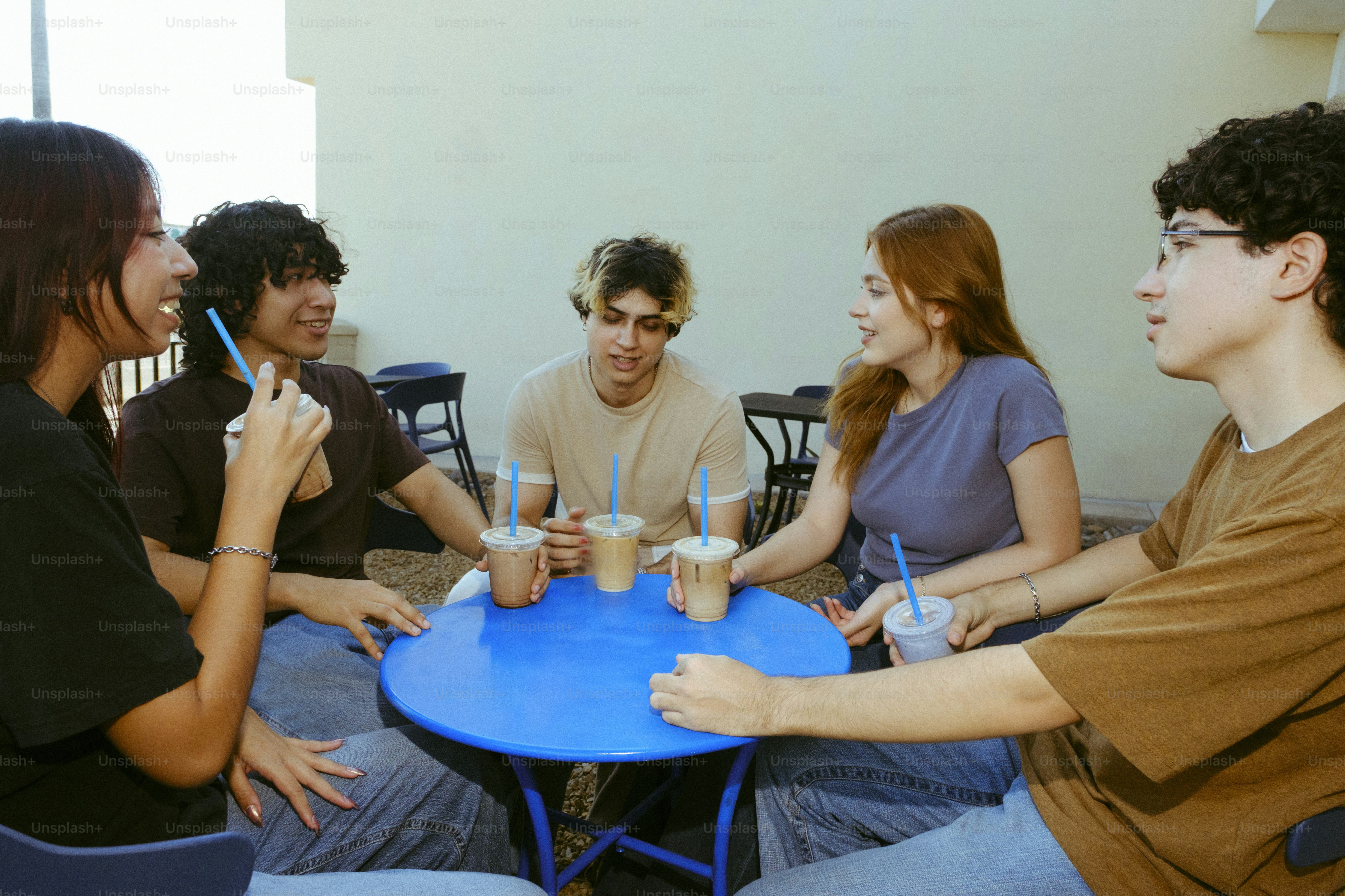 5人の若者が飲み物を飲みながら青いテーブルの周りに集まりました。