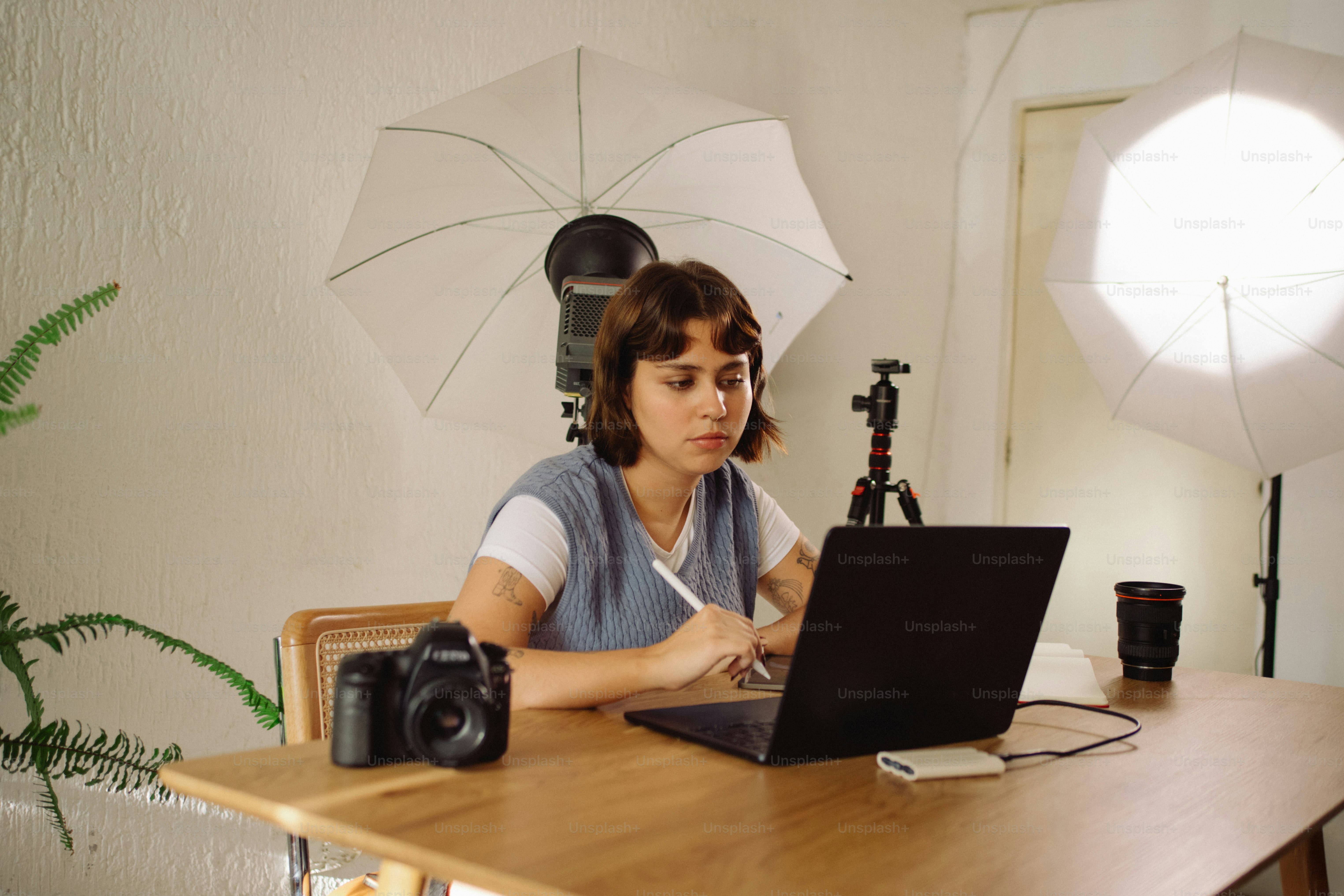 Woman working on laptop with camera and lighting equipment.