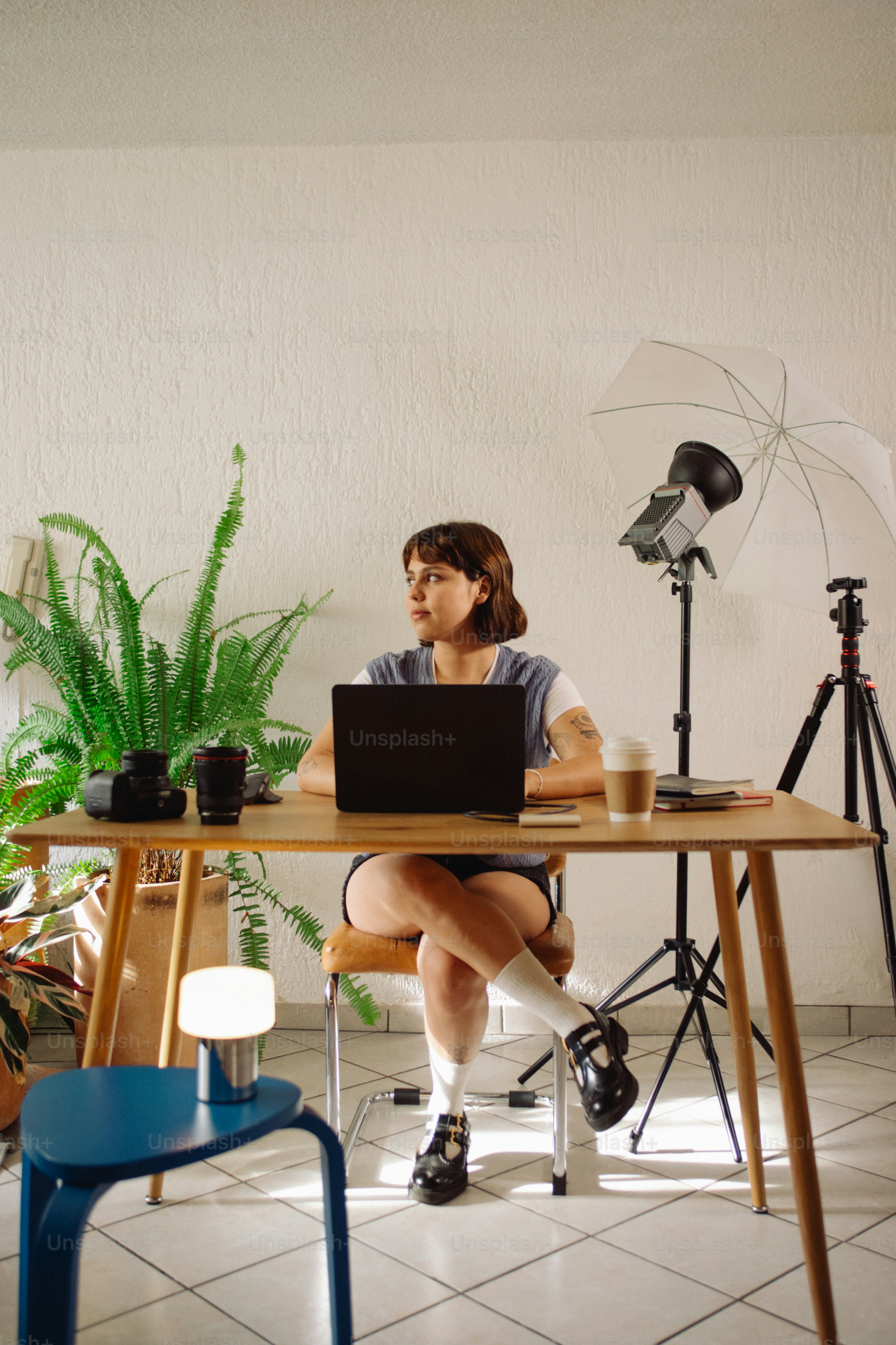 Woman working at desk with laptop and camera equipment.