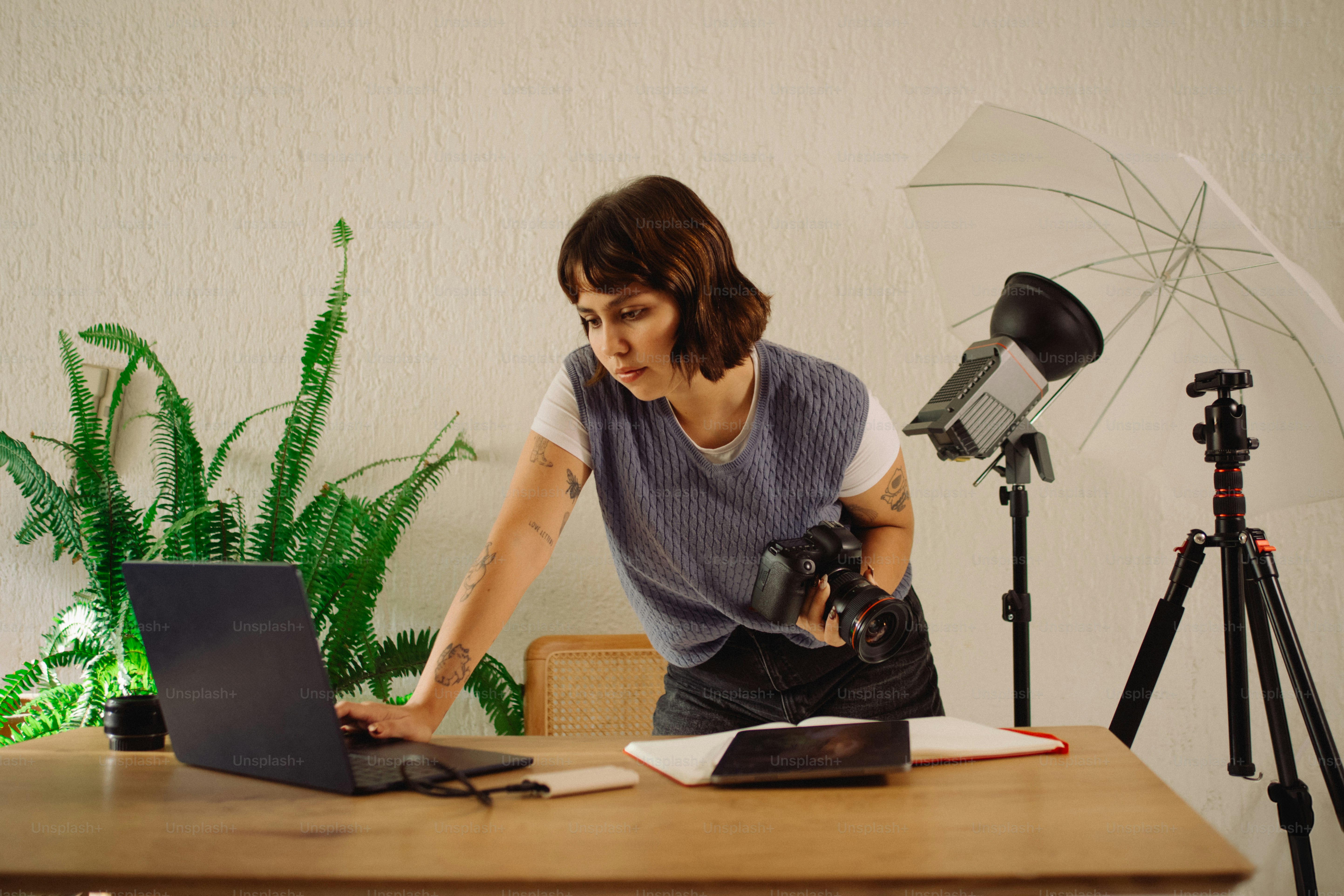 Woman with camera works on laptop near studio lighting.
