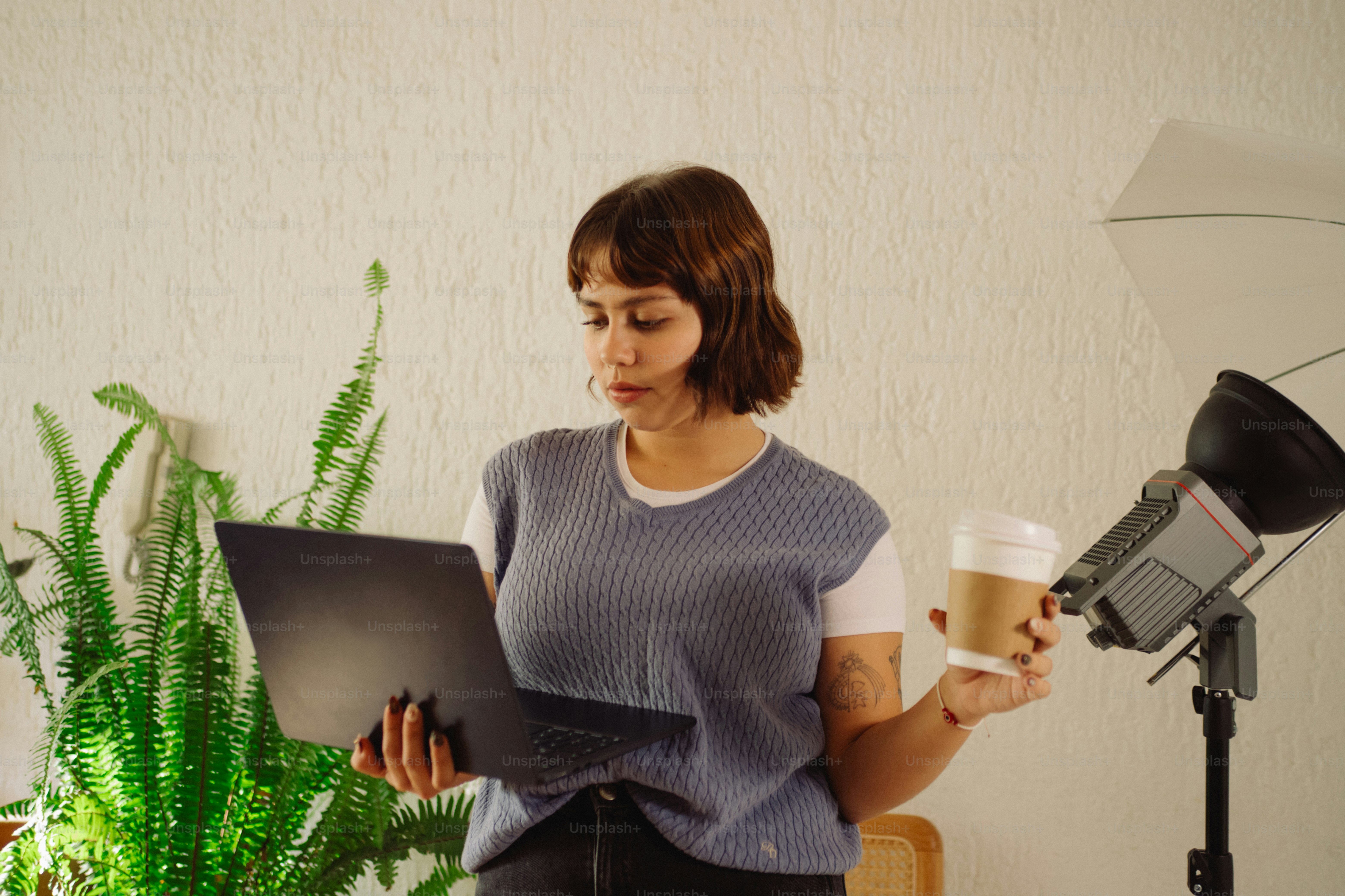 Woman with laptop and coffee cup near plant.