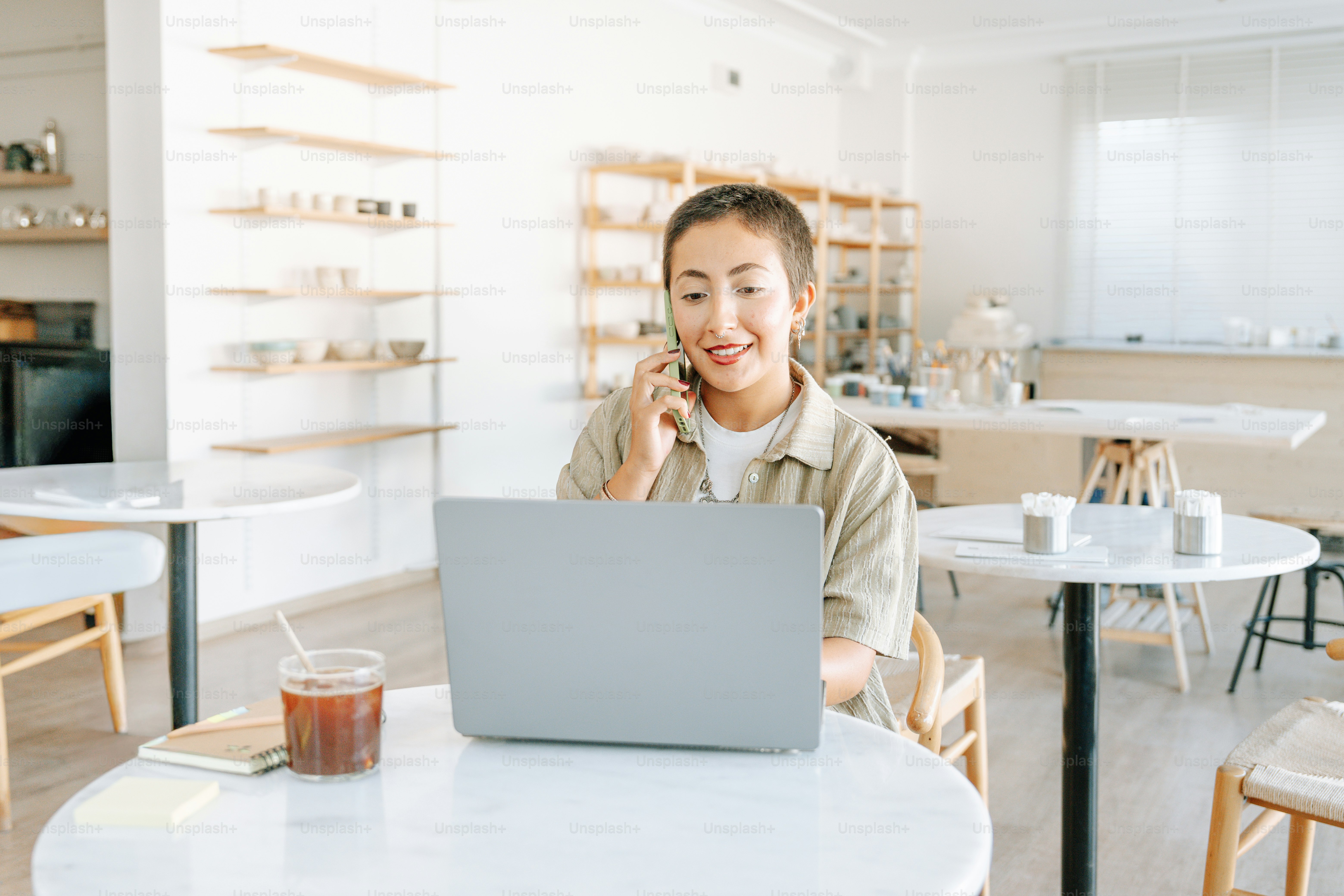 Woman on phone using laptop at cafe table.