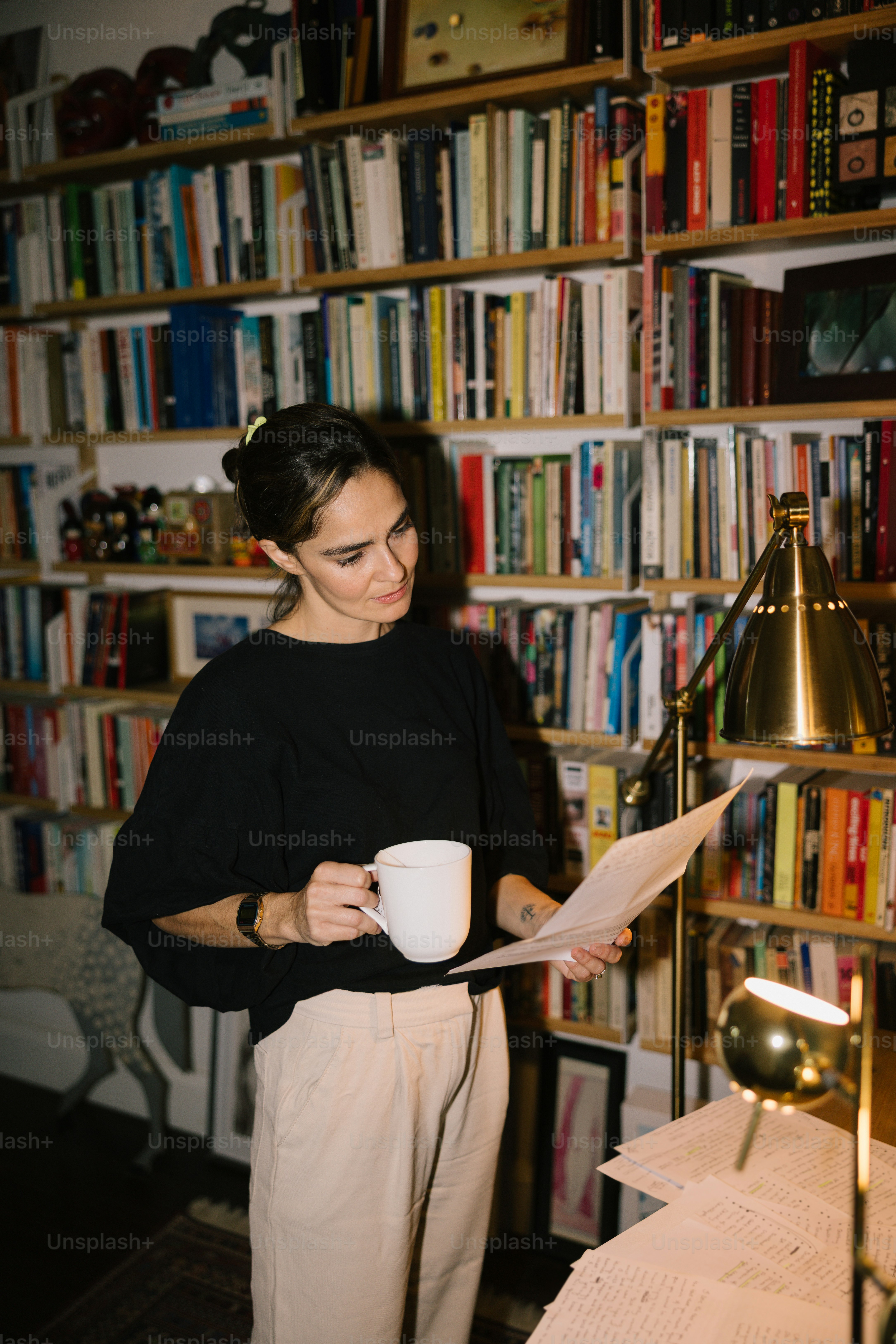 Woman holding coffee mug reading papers by bookshelves