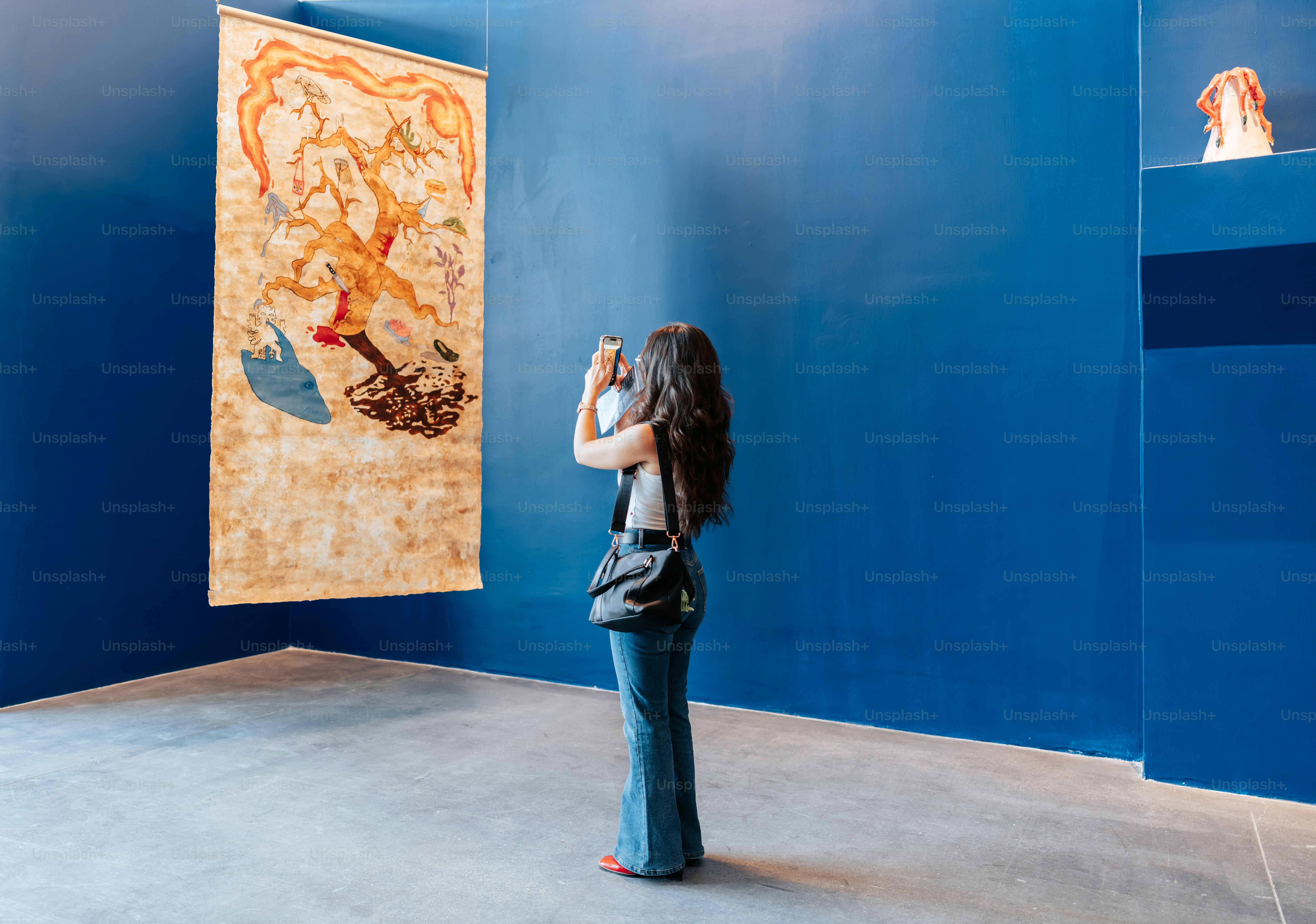 Woman photographing ancient tapestry on blue wall.