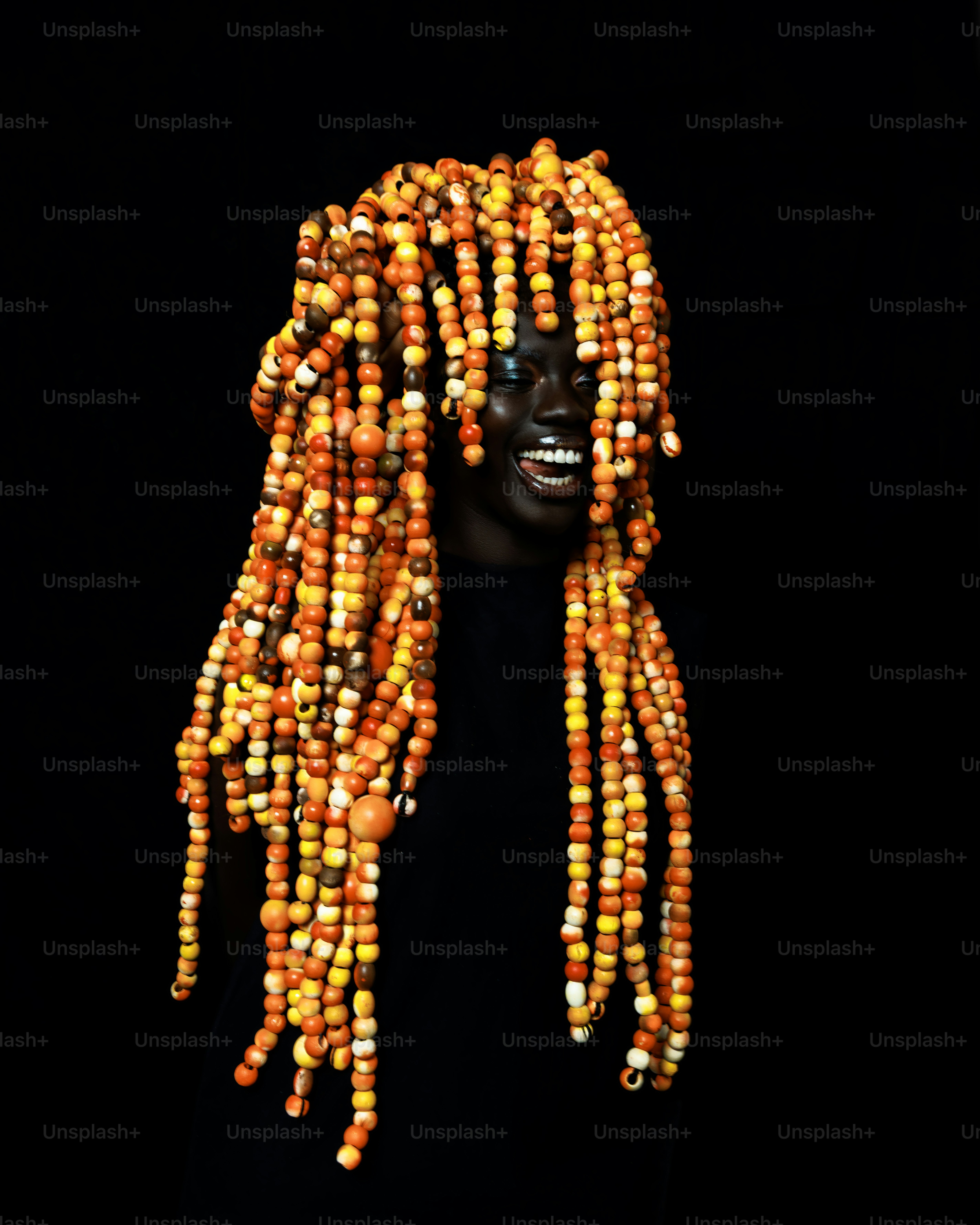 Eine Person mit kunstvoll perlenbesetzten Dreadlocks und einem breiten Lächeln.