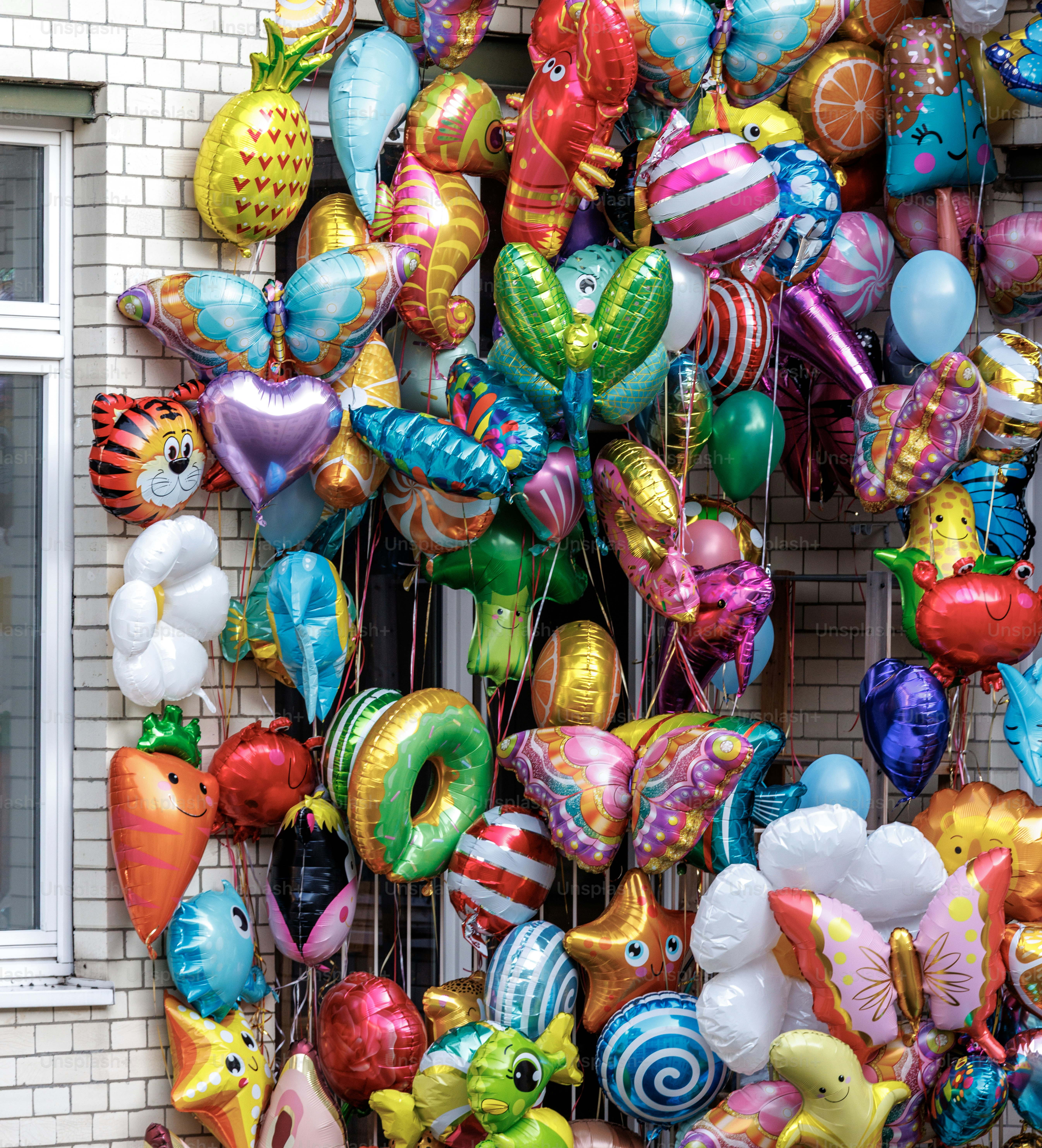 Assortiment de ballons en aluminium colorés sur un mur de briques.