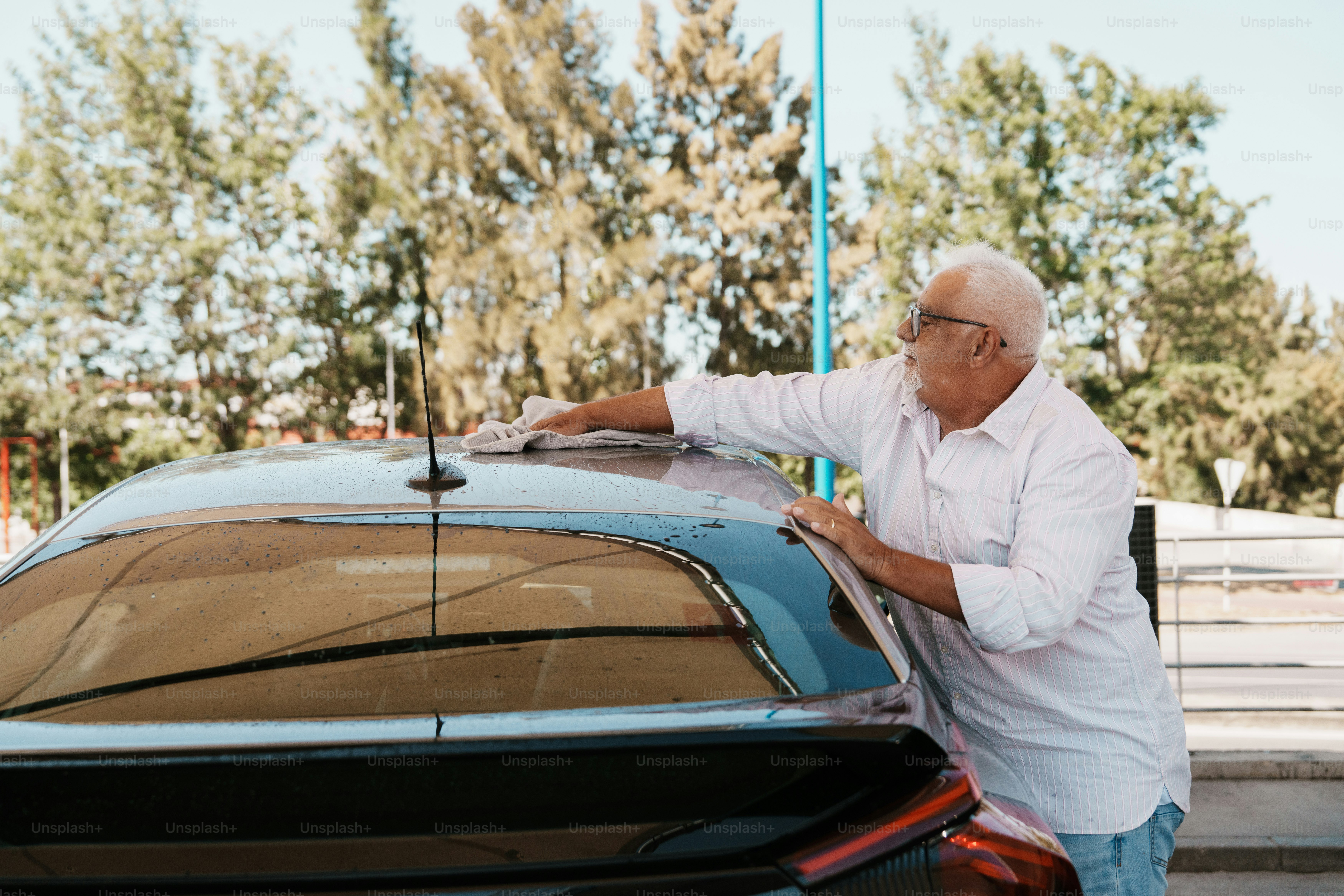 Homme âgé lavant une voiture avec un chiffon.