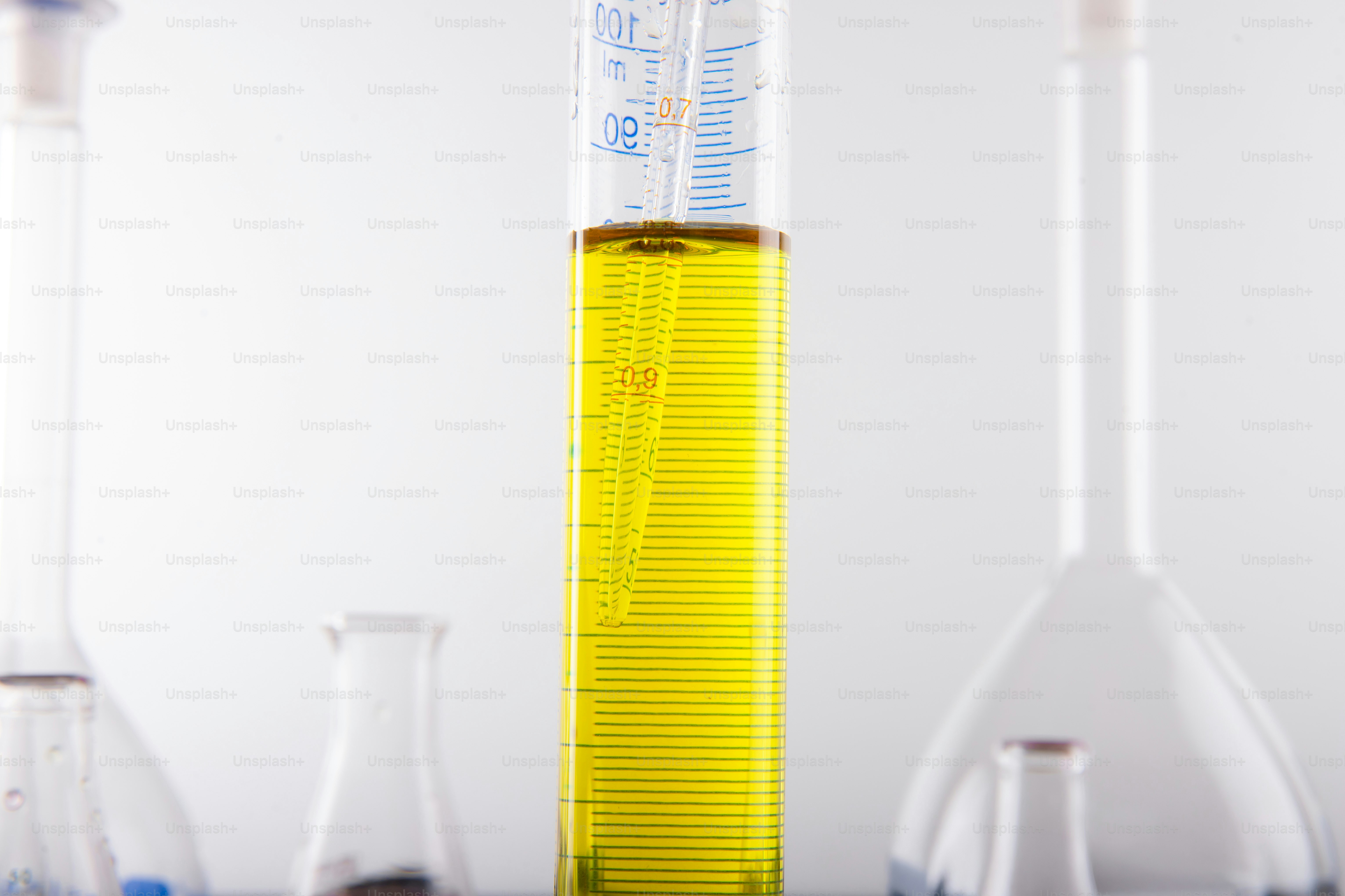 Yellow liquid in a graduated cylinder with lab equipment.