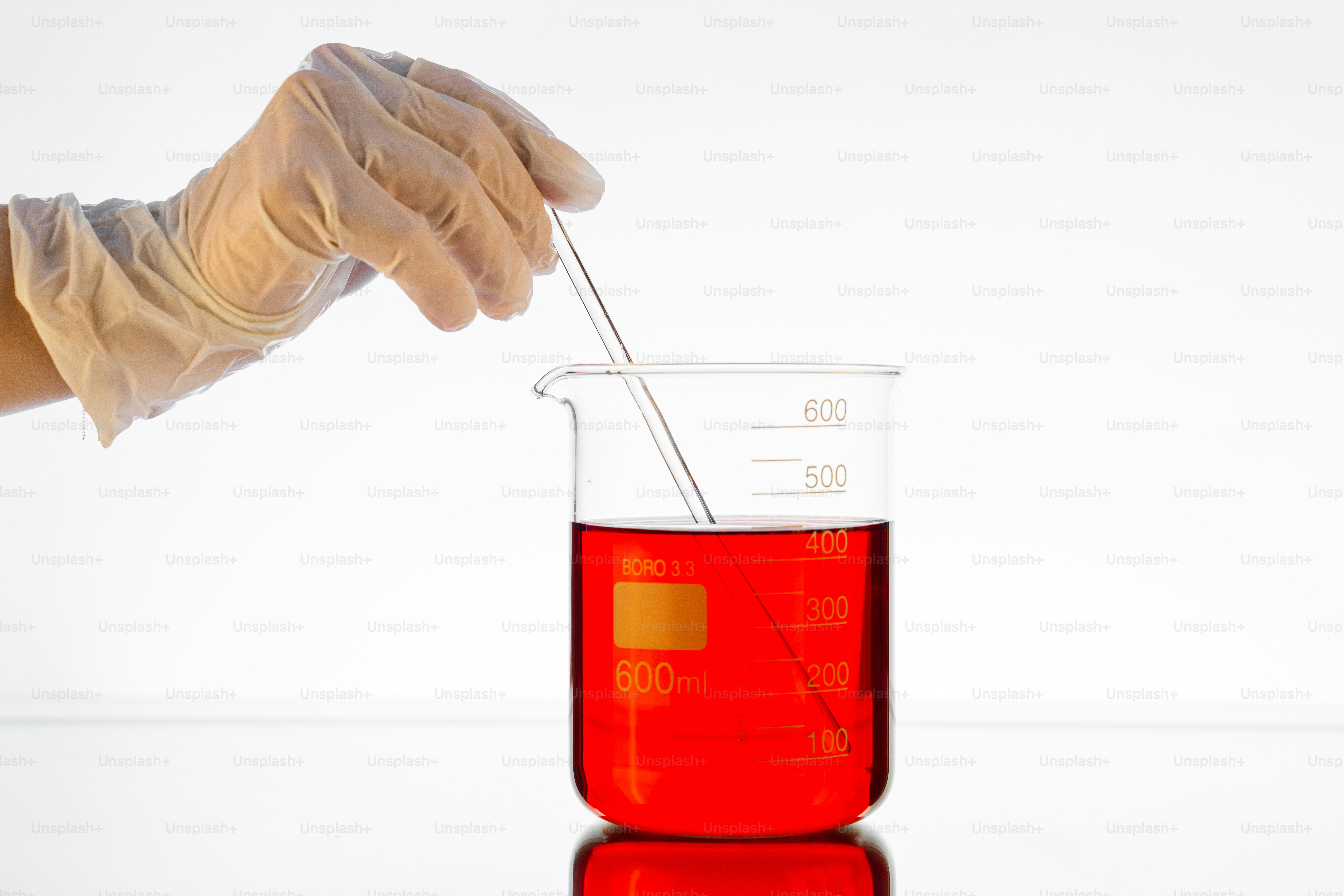 Hand in glove stirring red liquid in beaker.