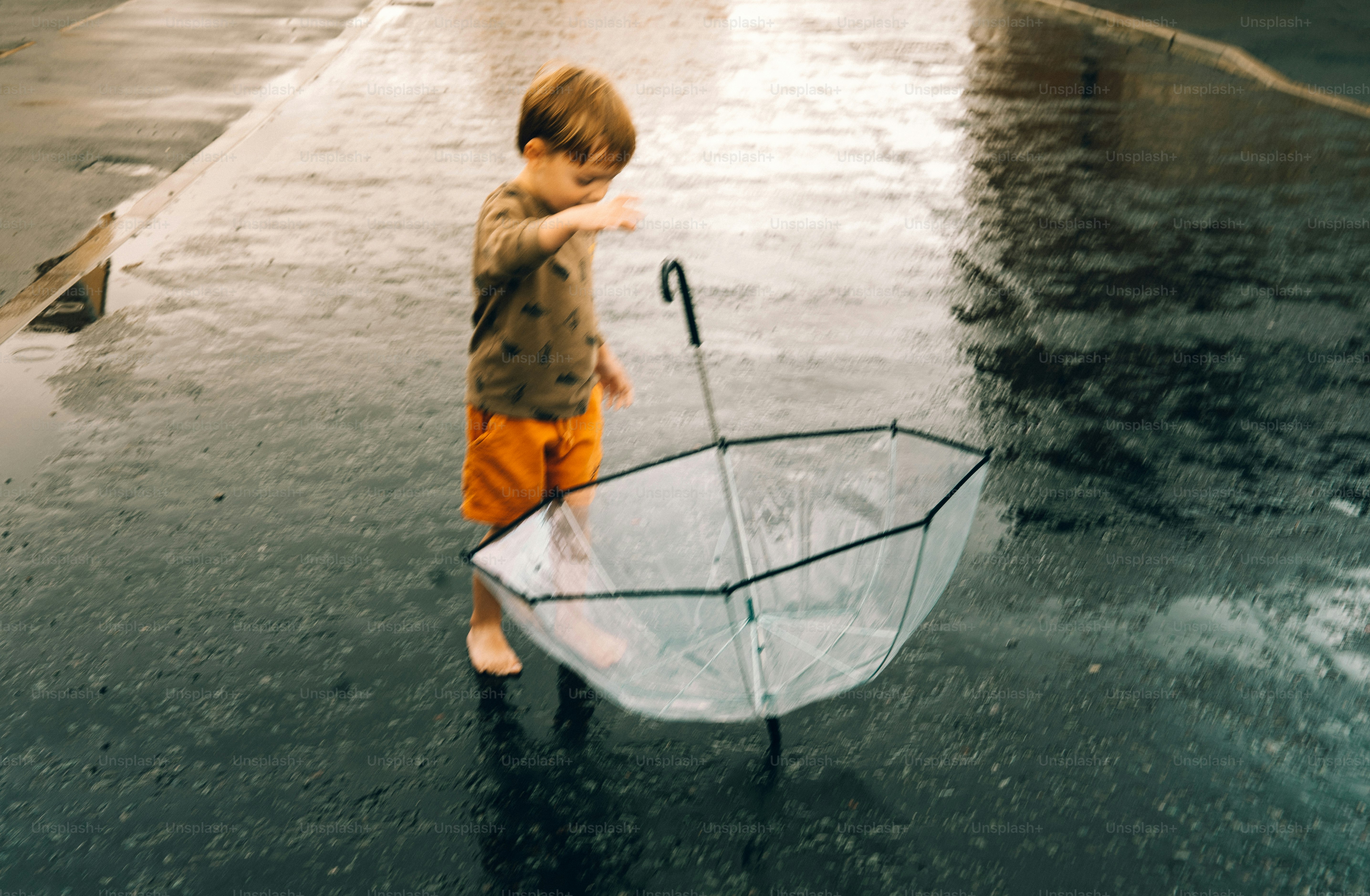 A young boy plays with an umbrella in the rain.