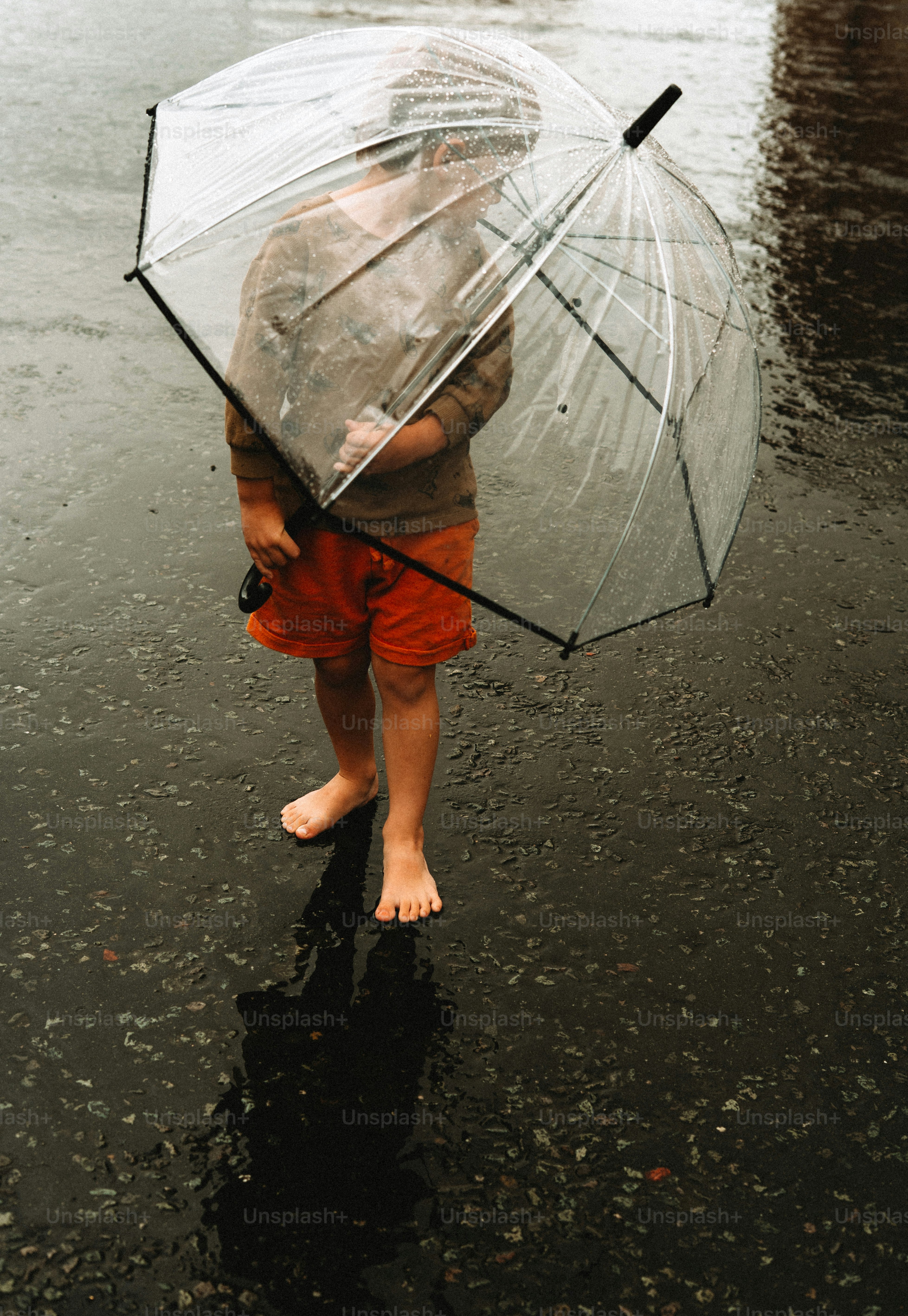 Barefoot child holding a clear umbrella in the rain