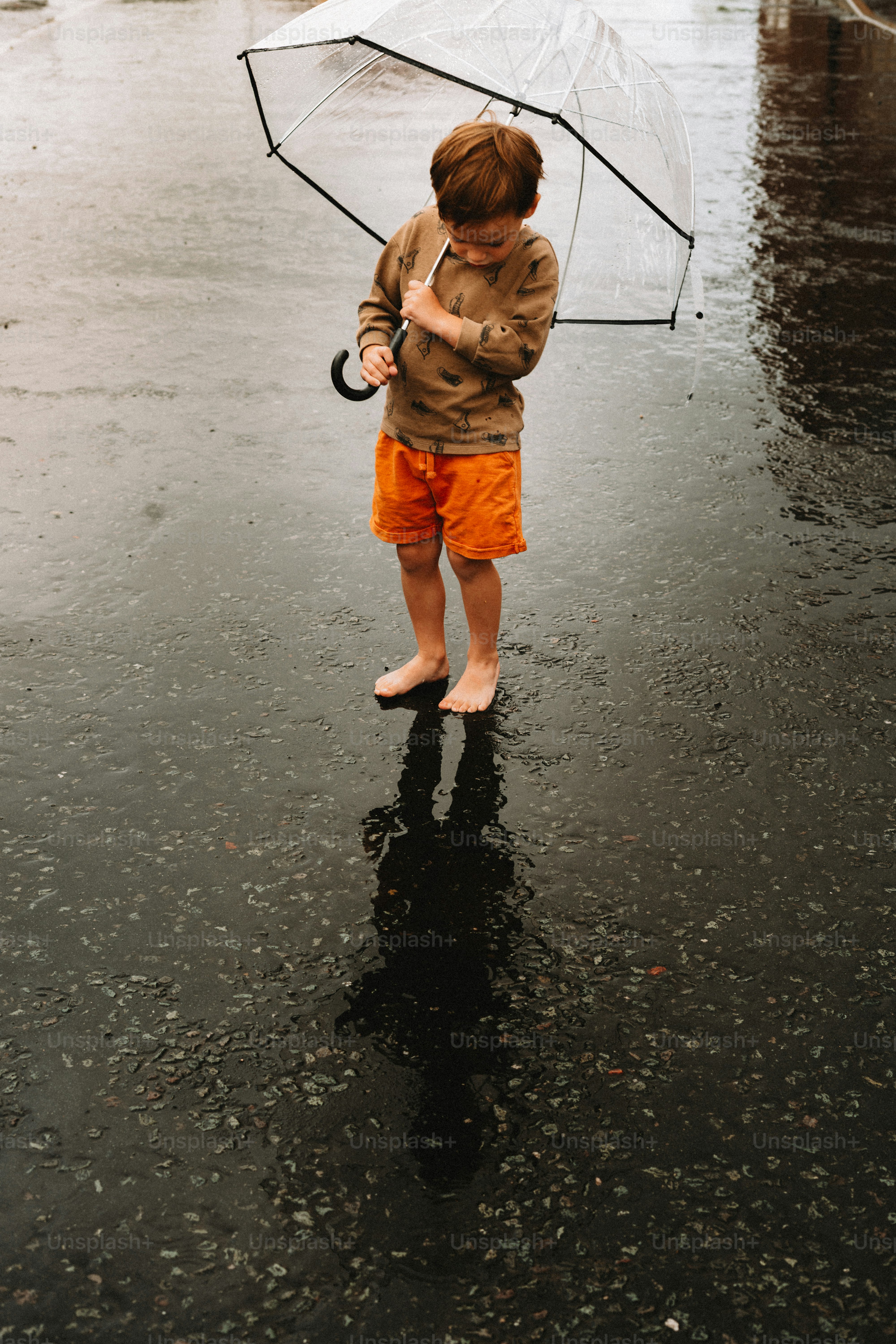 A young boy holds an umbrella in the rain.